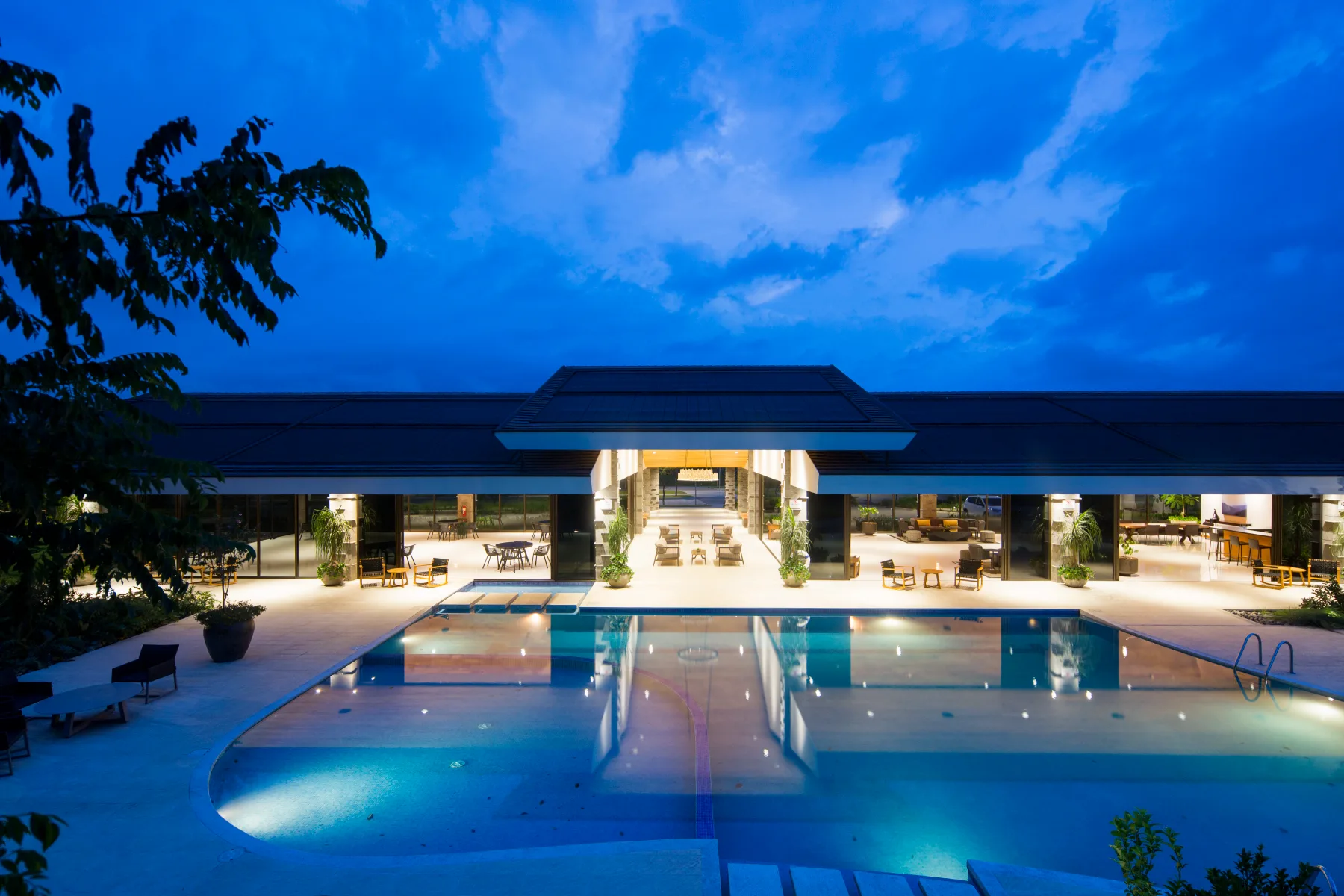 Representative hotel space: An illuminated outdoor pool sits in front of a low, modern building at dusk.