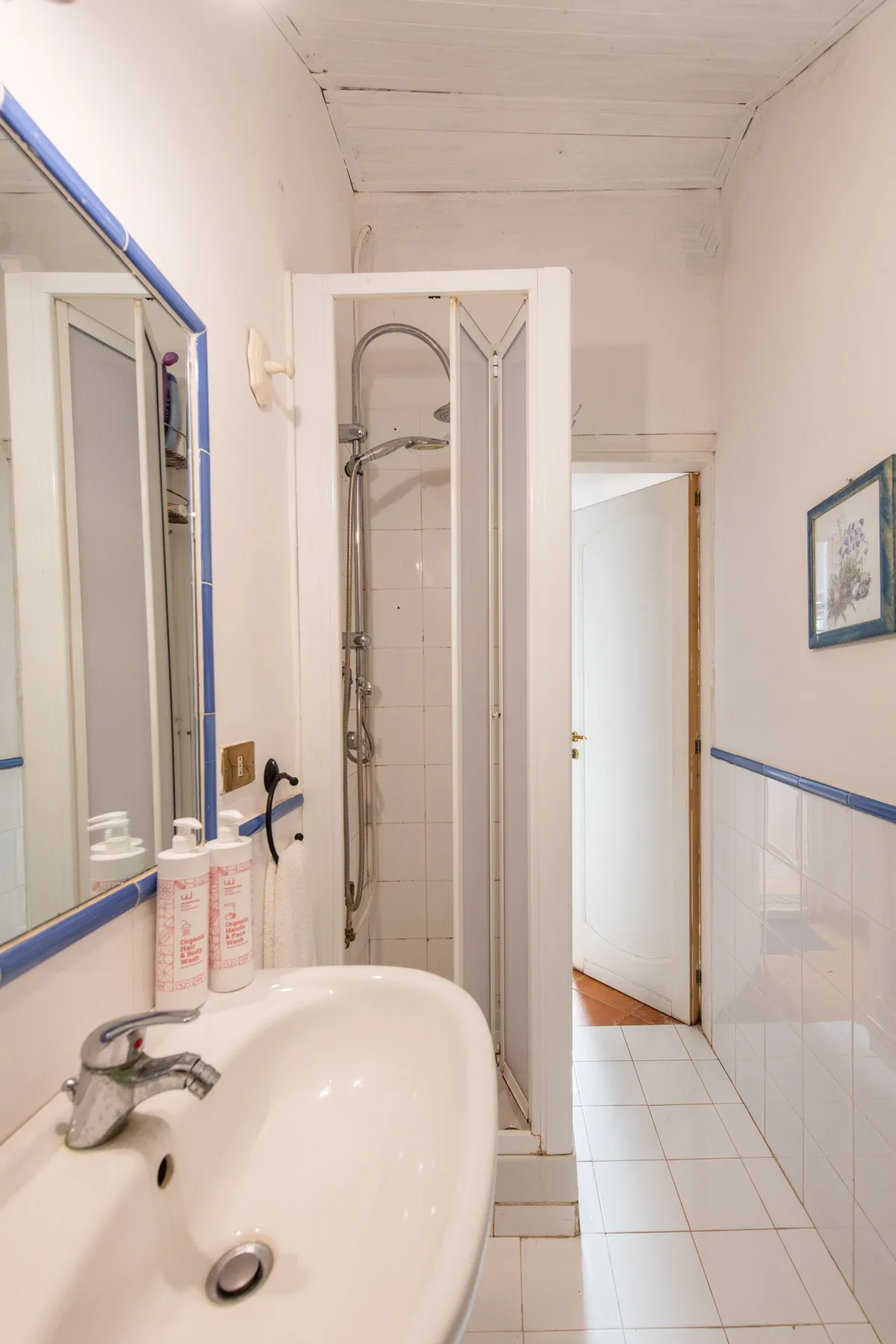 Un baño estrecho con un lavabo en primer plano y una ducha detrás.
