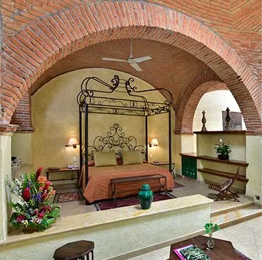 Espacio representativo del hotel: Dormitorio con una cama de metal ornamentada bajo un arco de ladrillo.