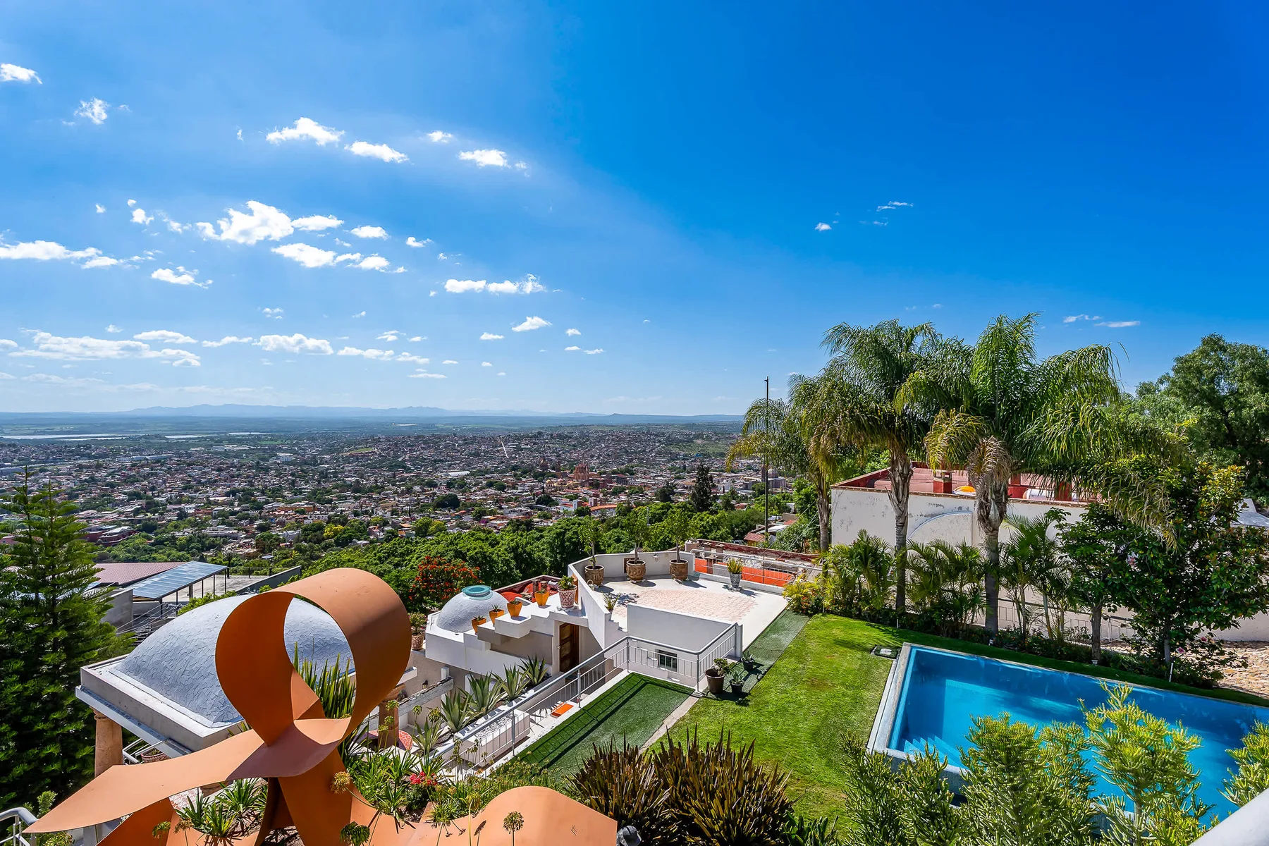 A hillside property overlooks a sprawling city, with a swimming pool in the foreground.