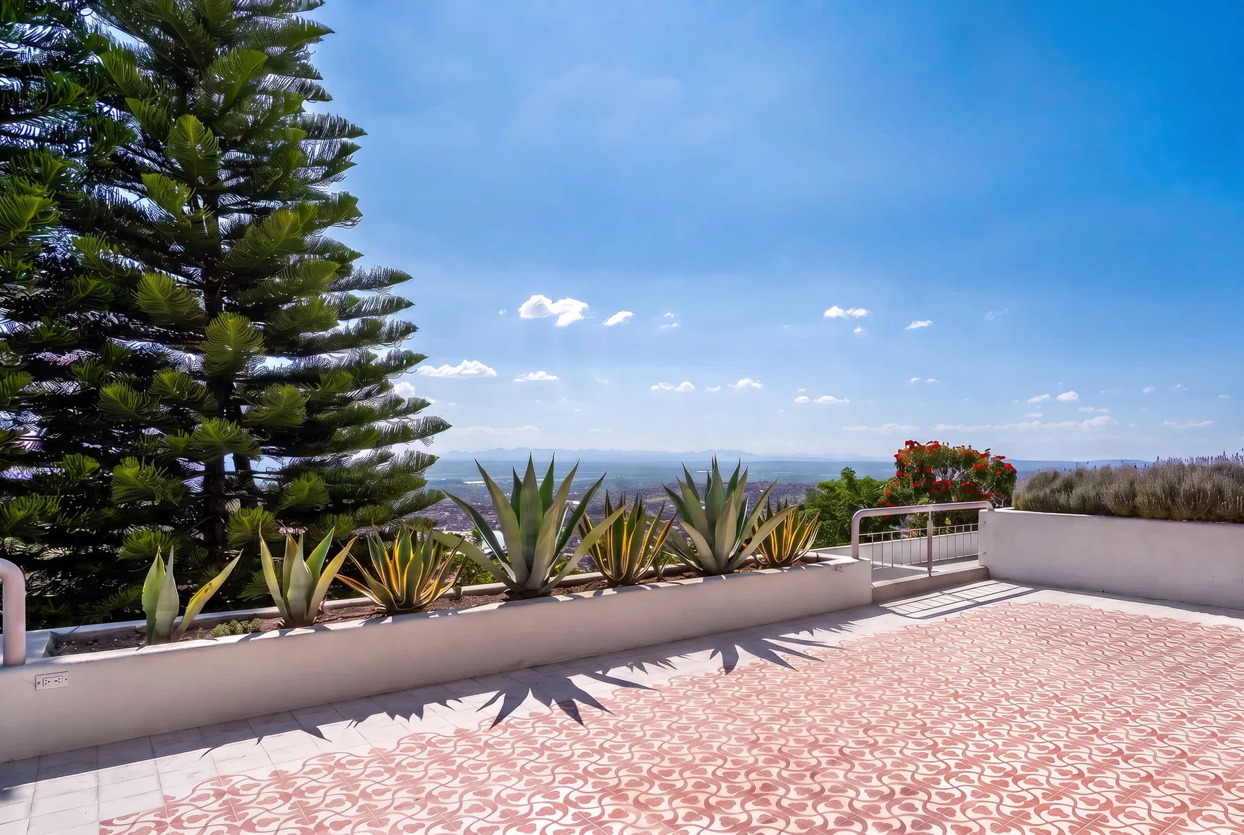 A sunlit terrace overlooks a distant landscape, with plants lining the edge.
