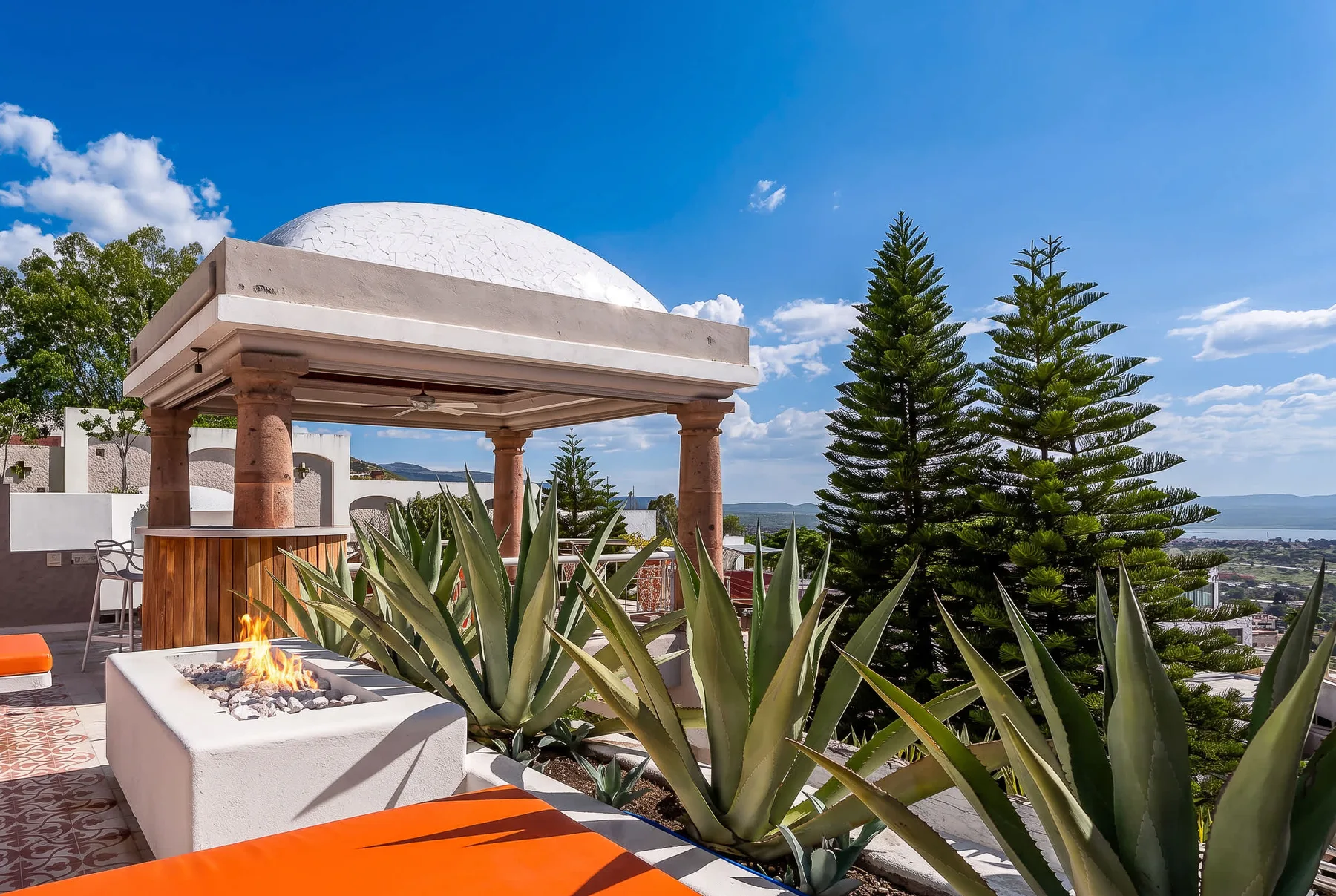 An outdoor terrace features a fire pit, lounge seating, and a view across the landscape.