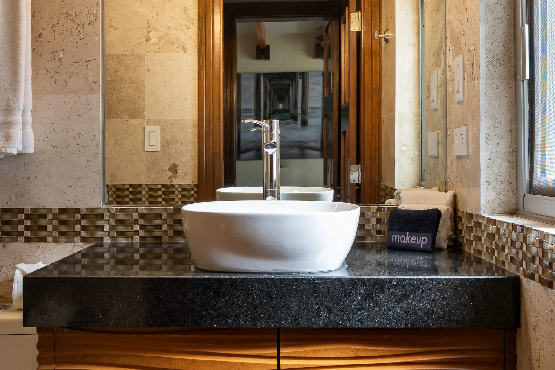 A bathroom vanity features a white vessel sink on a dark countertop.