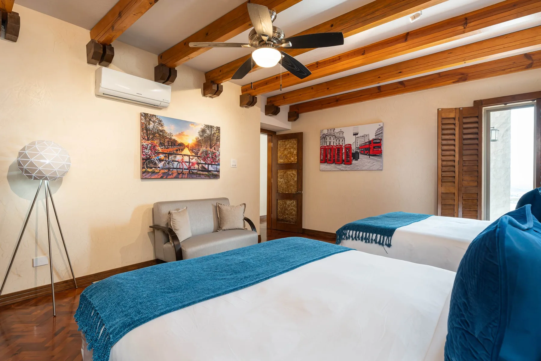 A bedroom with two beds, exposed wooden ceiling beams, and a ceiling fan.