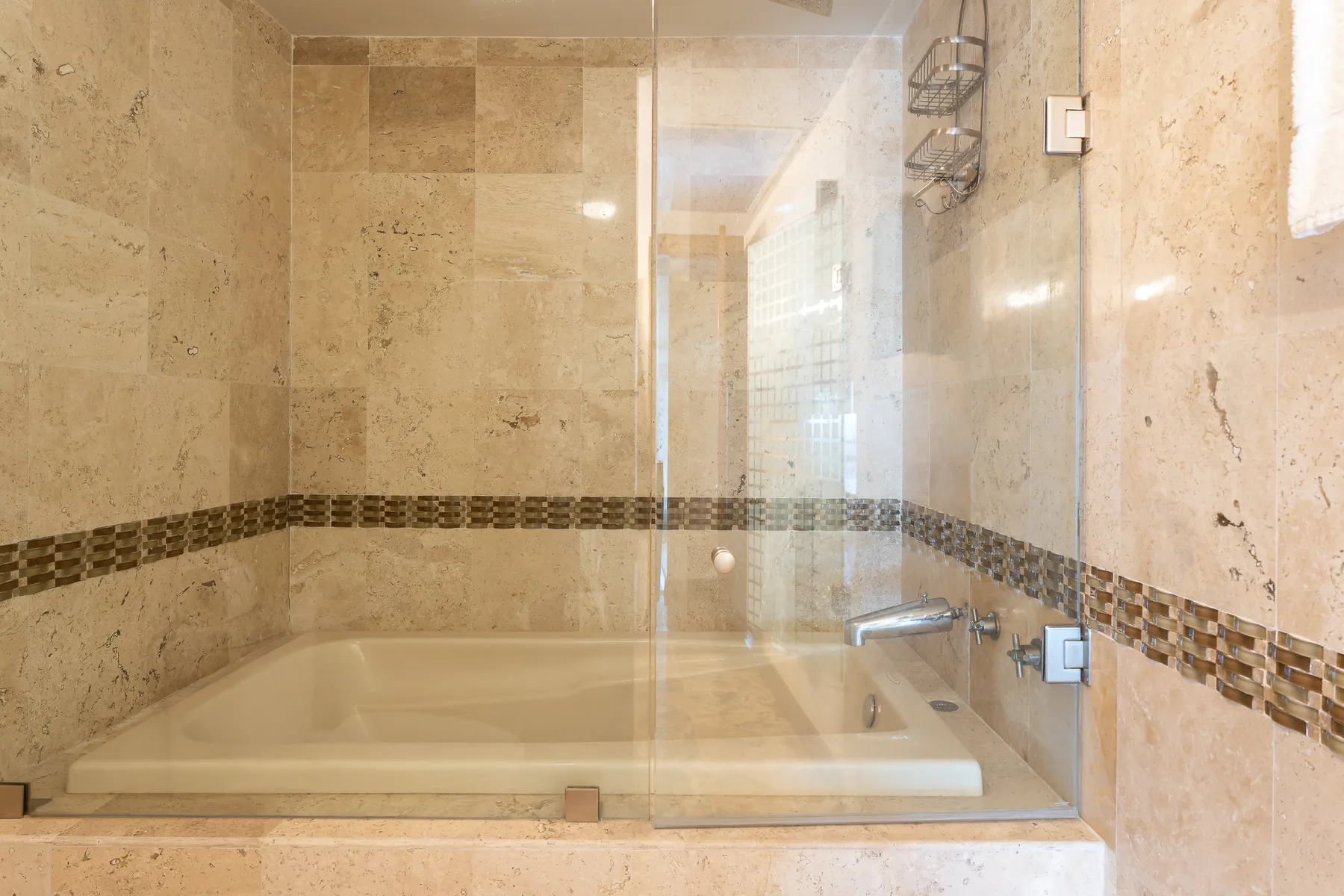 A tiled bathroom with a bathtub behind a glass shower screen.