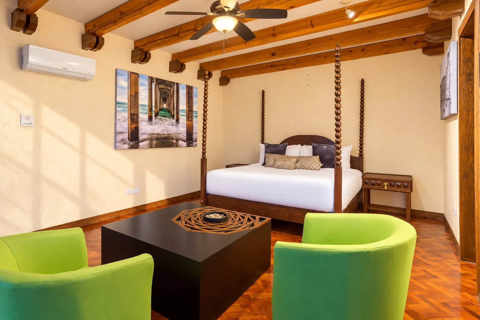 A bedroom with a four-poster bed, a dark coffee table, and green seating.