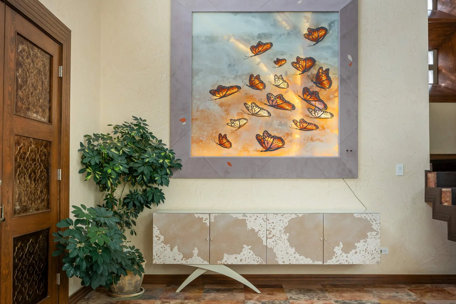 A hallway with framed butterfly artwork above a wall-mounted cabinet and a leafy plant.