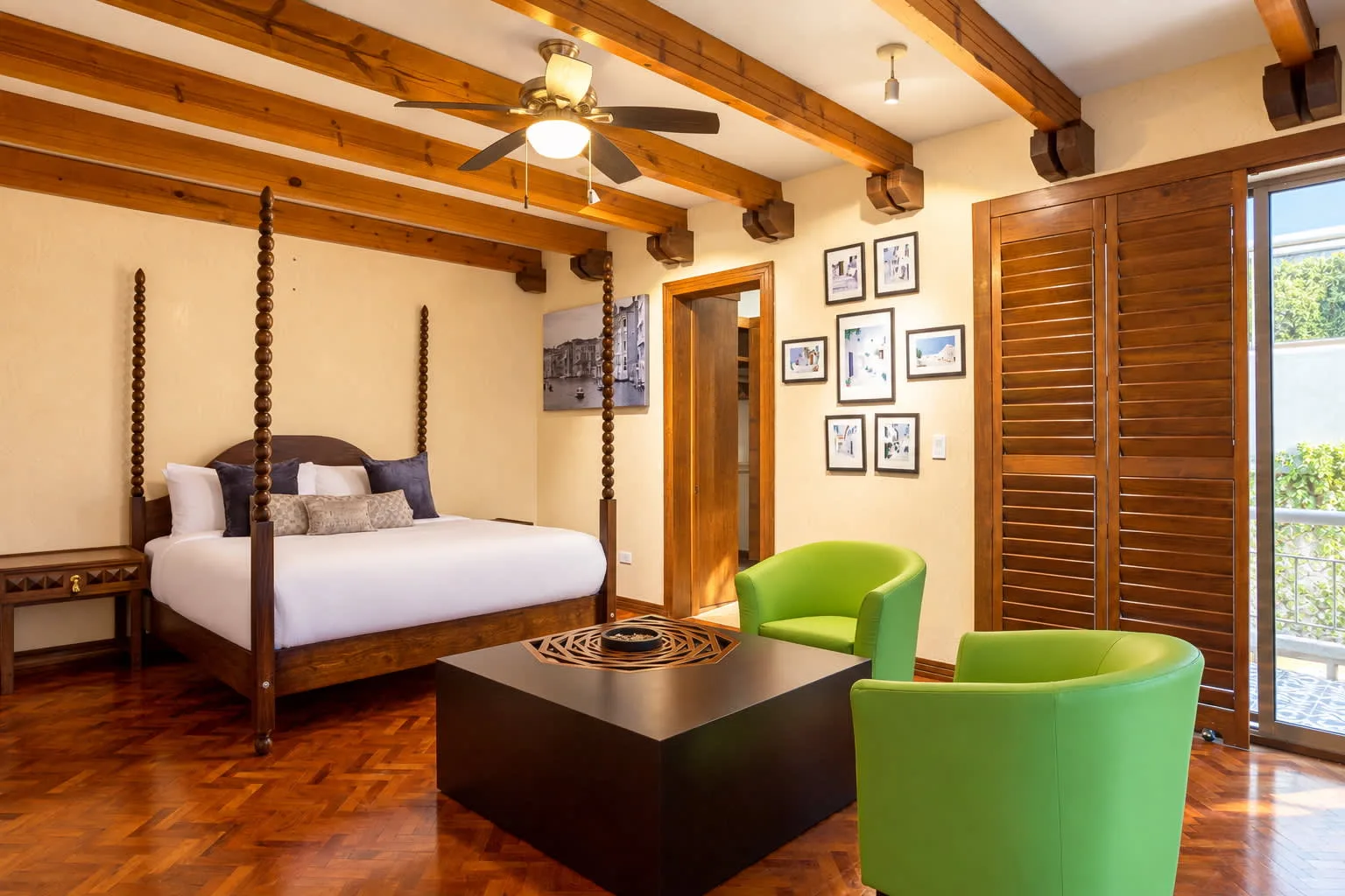 A bedroom with a four-poster bed, green seating, and exposed wooden ceiling beams.