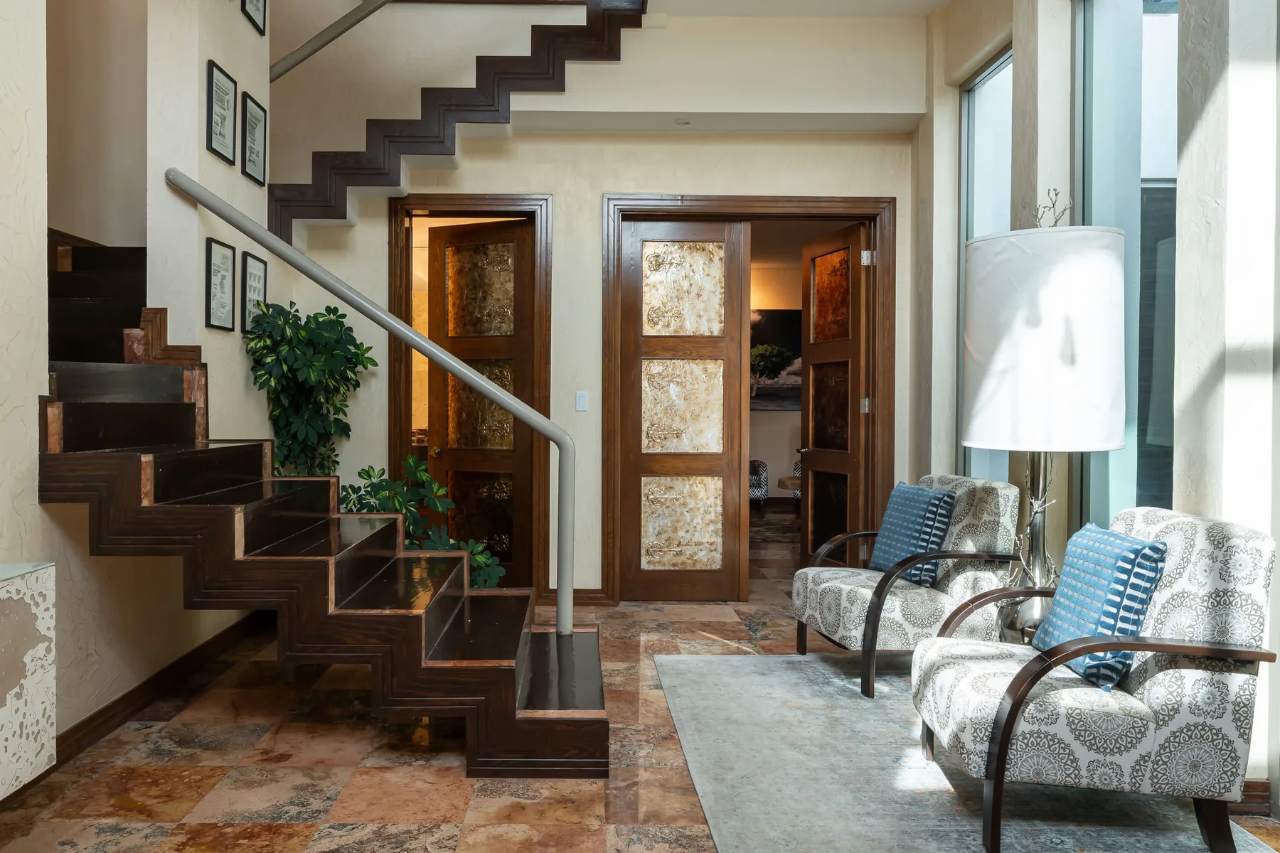 A living area with a dark wooden staircase, patterned seating, and tall windows.
