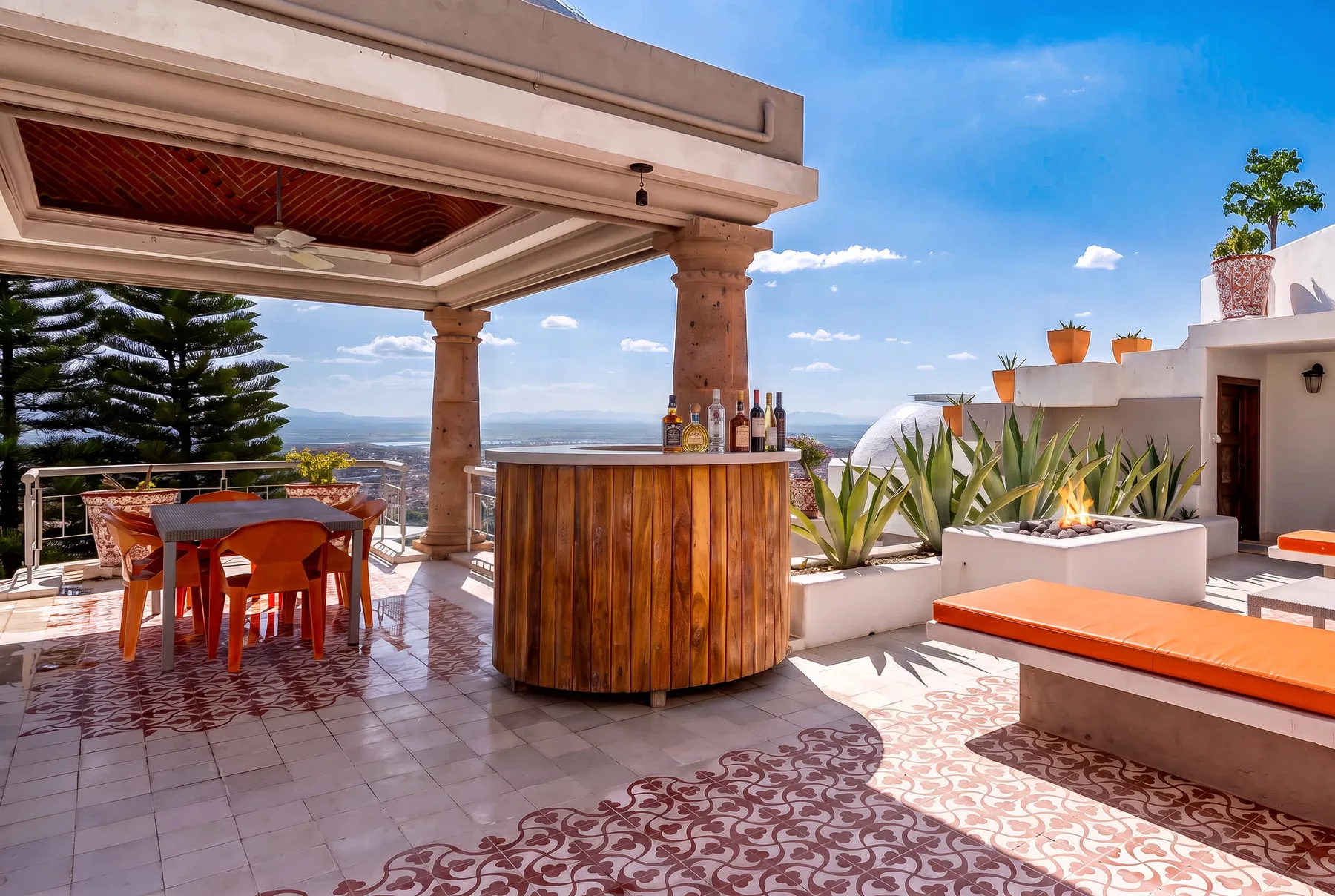 An outdoor terrace with a wooden bar, dining table, and cushioned seating.