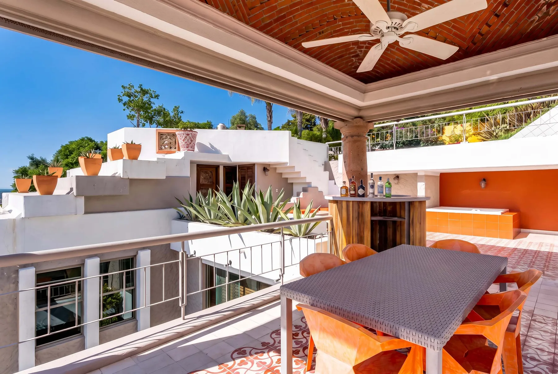 A covered rooftop terrace has a dining table and a built-in bar.