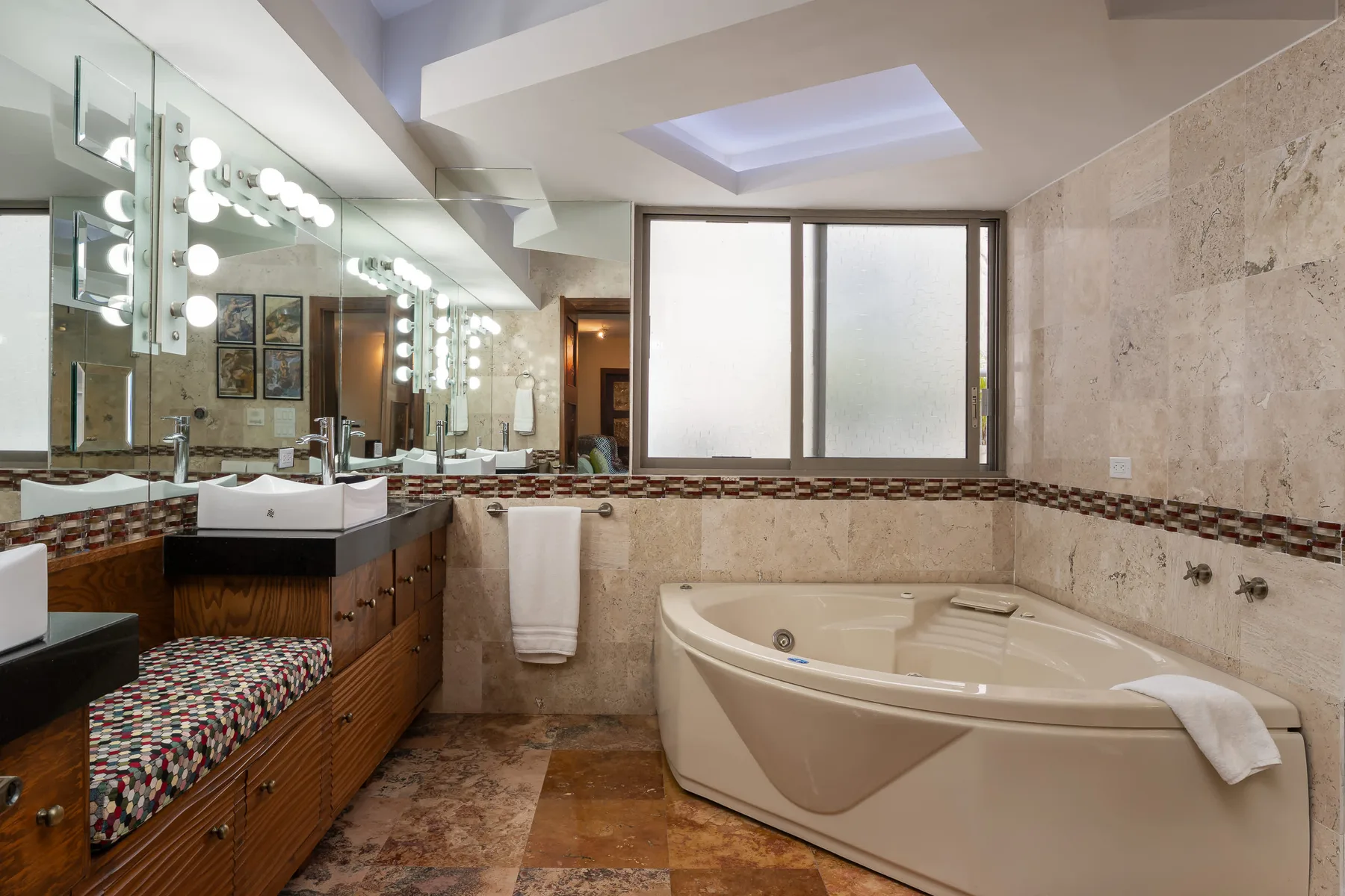 A bathroom with a large bathtub and a long vanity beneath illuminated mirrors.