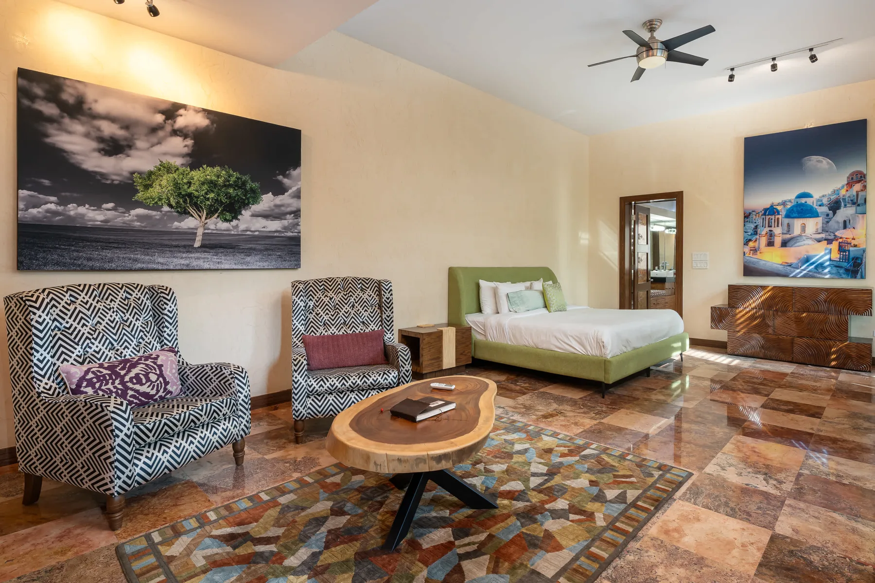 A bedroom with a bed, patterned seating, and colorful artwork.