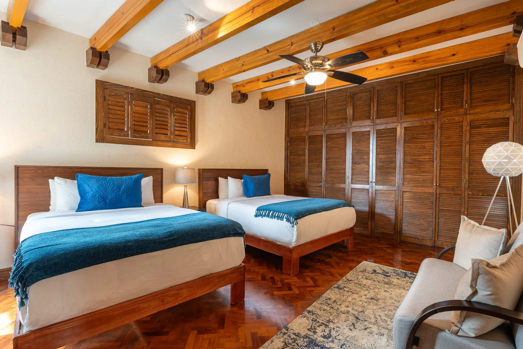 A bedroom with two beds, wooden ceiling beams, and a seating area.