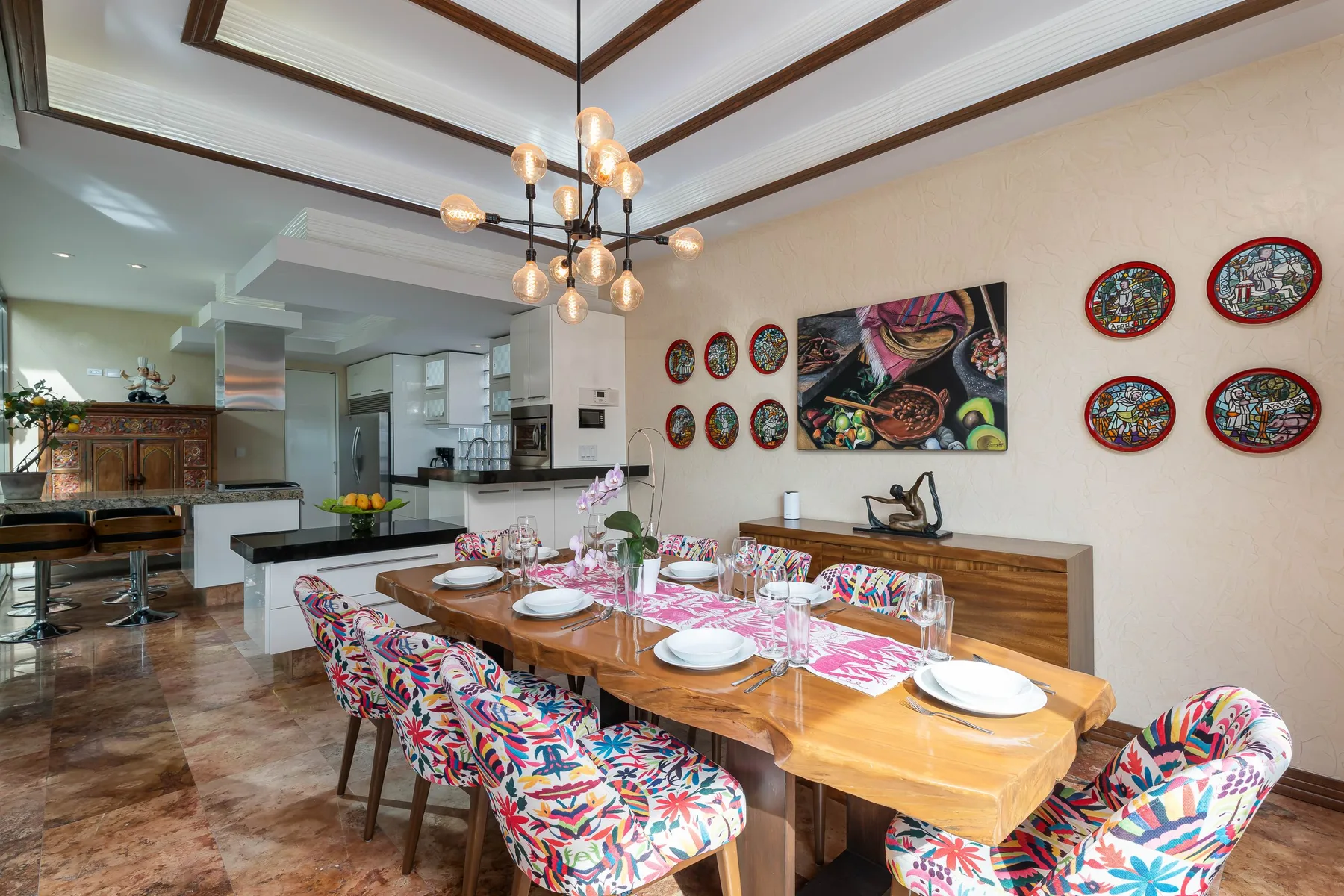Dining area with a long table set for a meal beside an open kitchen.