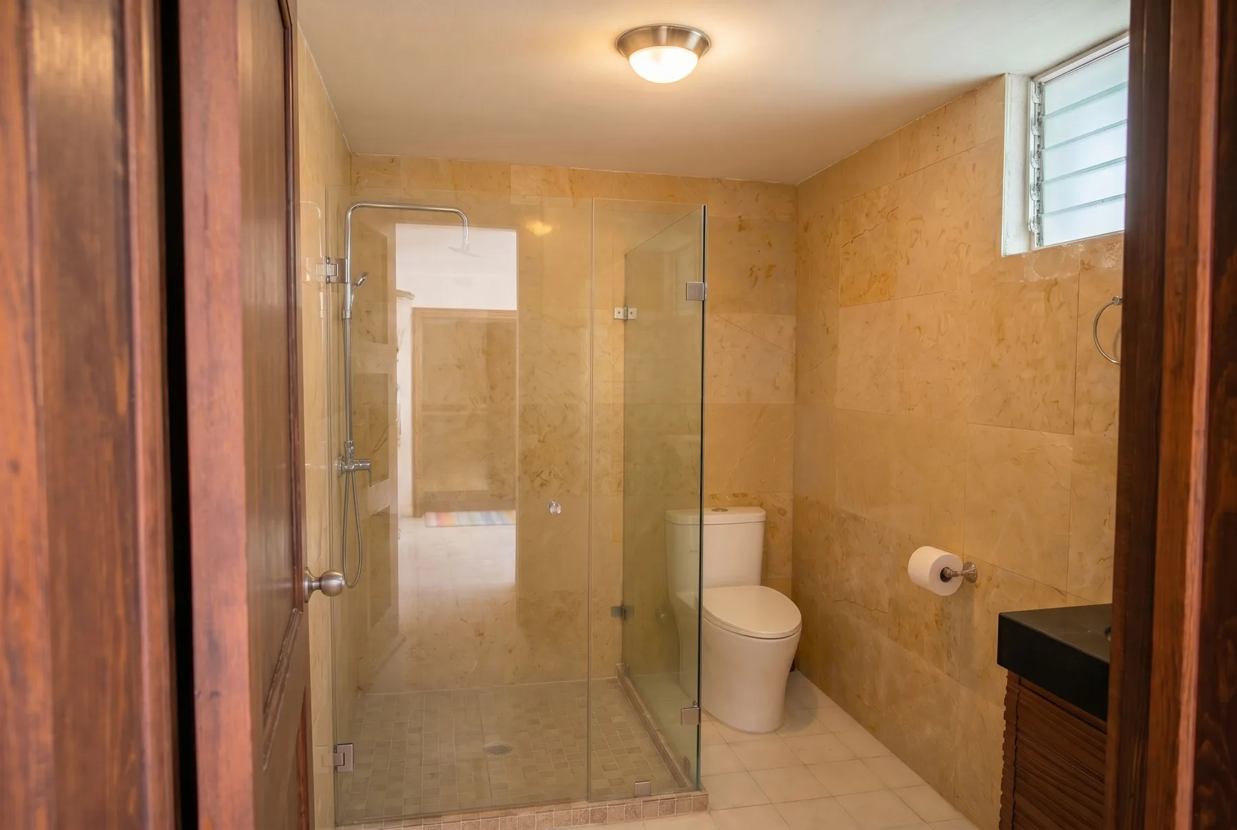 A tiled bathroom with a glass shower, toilet, and small window.