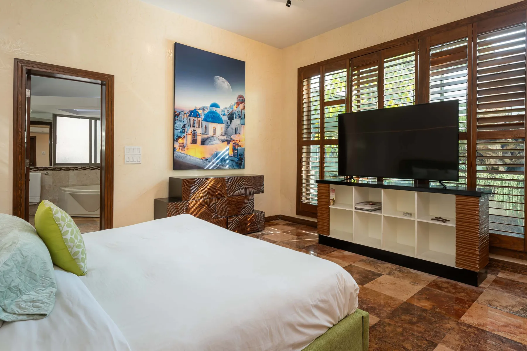 A bedroom with a bed, television, and wide windows with wooden shutters.