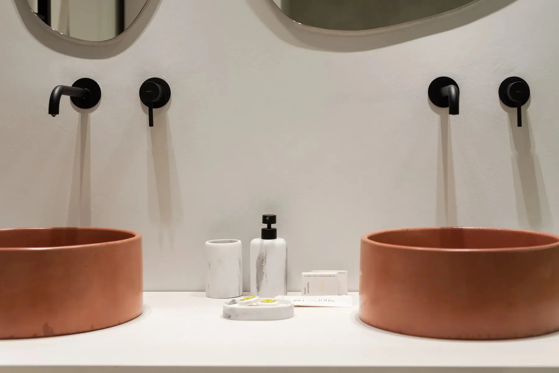 A bathroom vanity with two terracotta vessel sinks and black wall-mounted faucets.