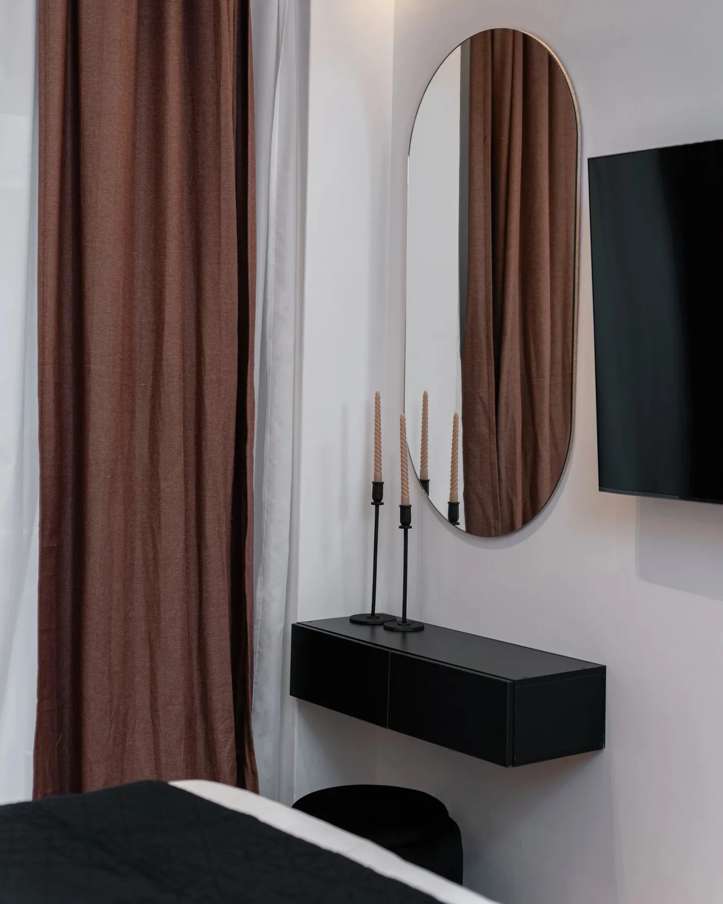 A bedroom corner with brown curtains, a wall mirror, and a floating console.