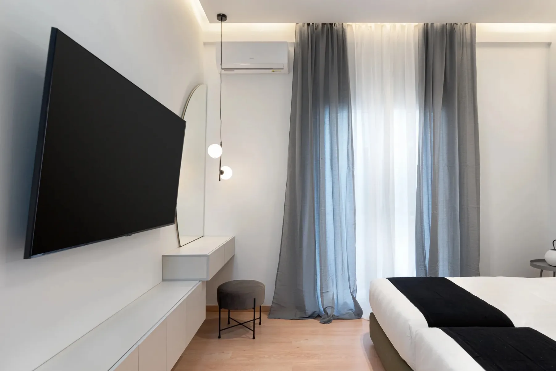 A bedroom with a bed, wall-mounted television, and curtains over the window.