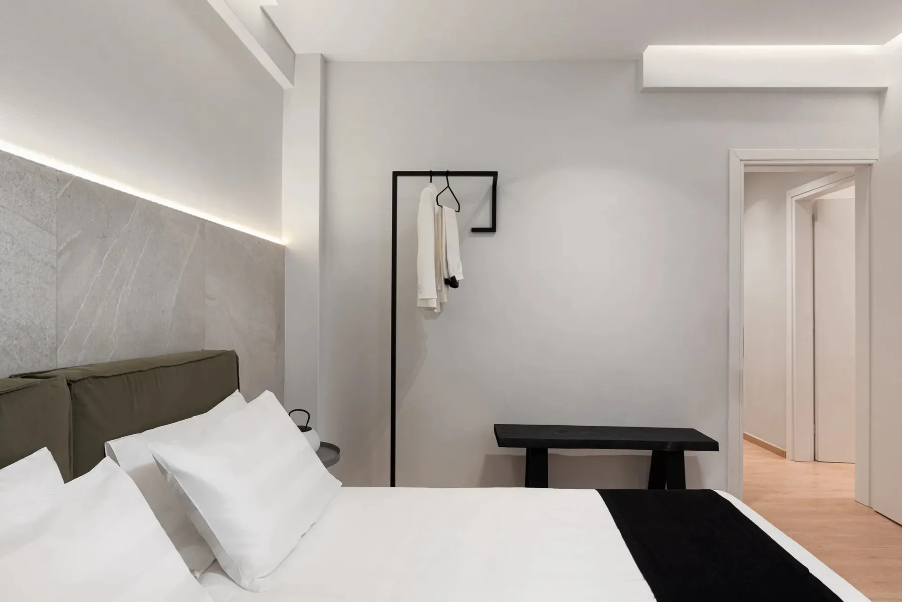 A bright bedroom with a bed, dark headboard, and a small bench.