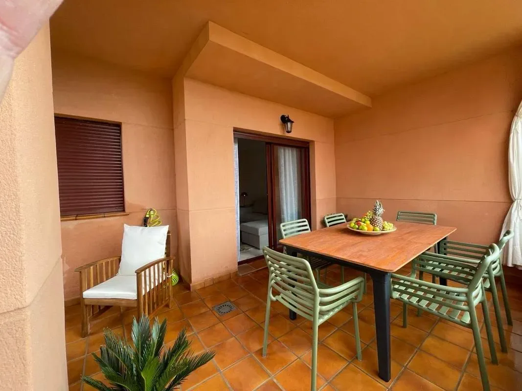 A covered patio has a dining table and seating beside a sliding glass door.