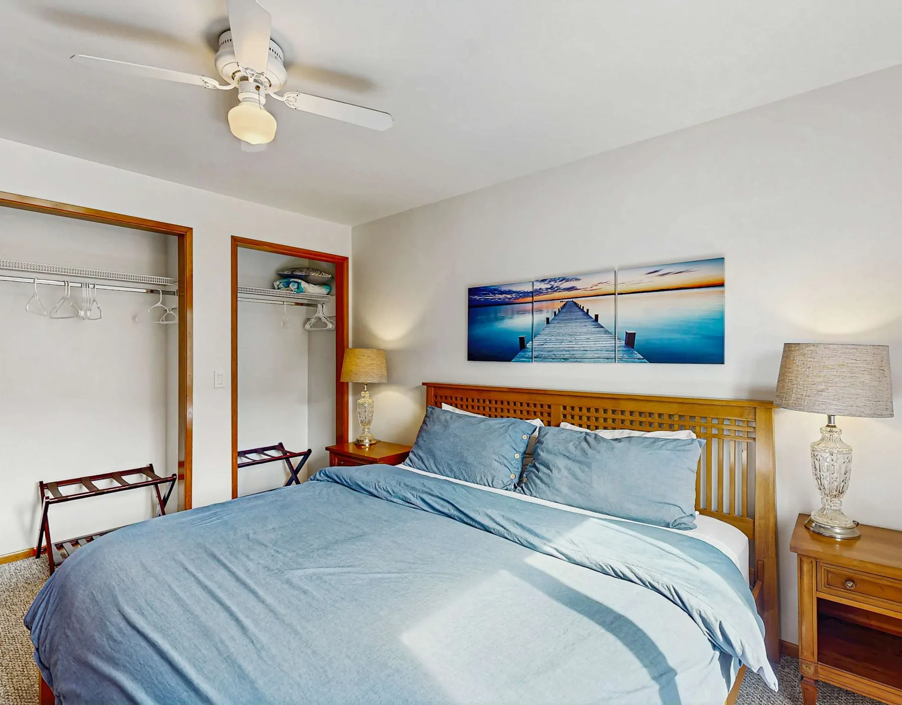 A bedroom with a bed beneath a wooden headboard and a beach picture on the wall.