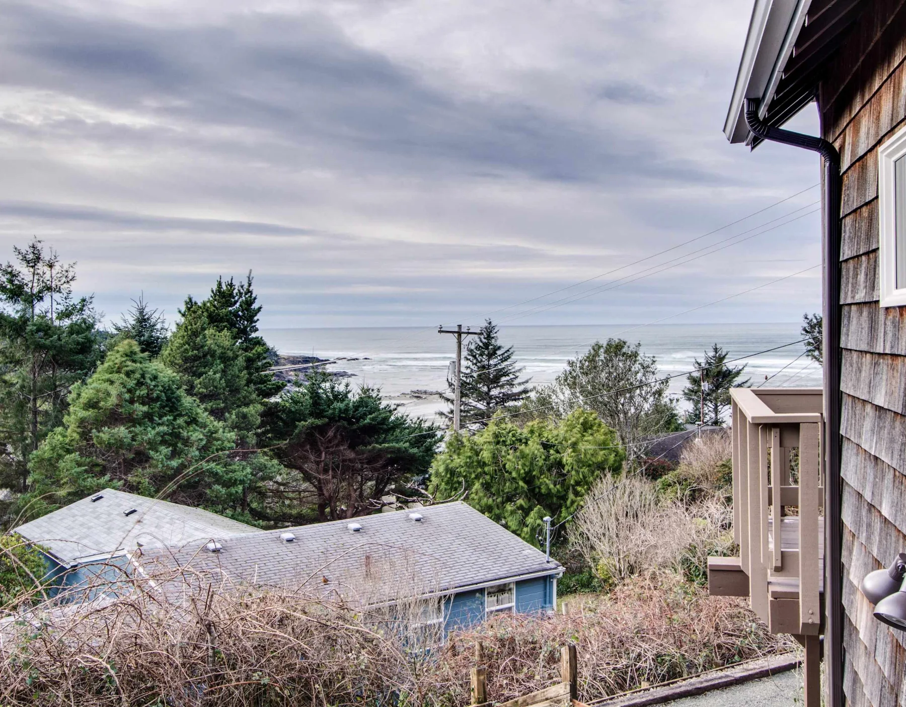 A coastal house exterior overlooks the ocean beyond trees and rooftops.