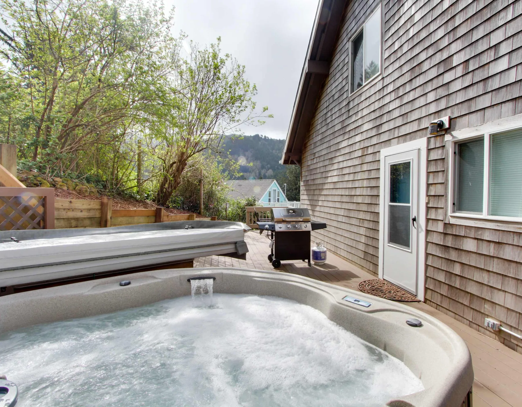 An outdoor hot tub sits beside a house on a wooden deck.