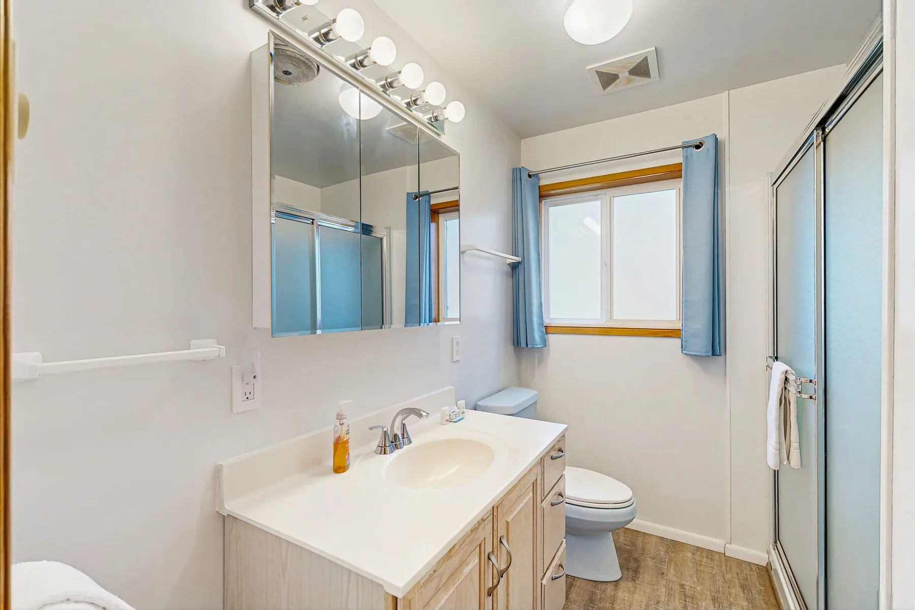 A bright bathroom with a vanity, mirror, toilet, and window.