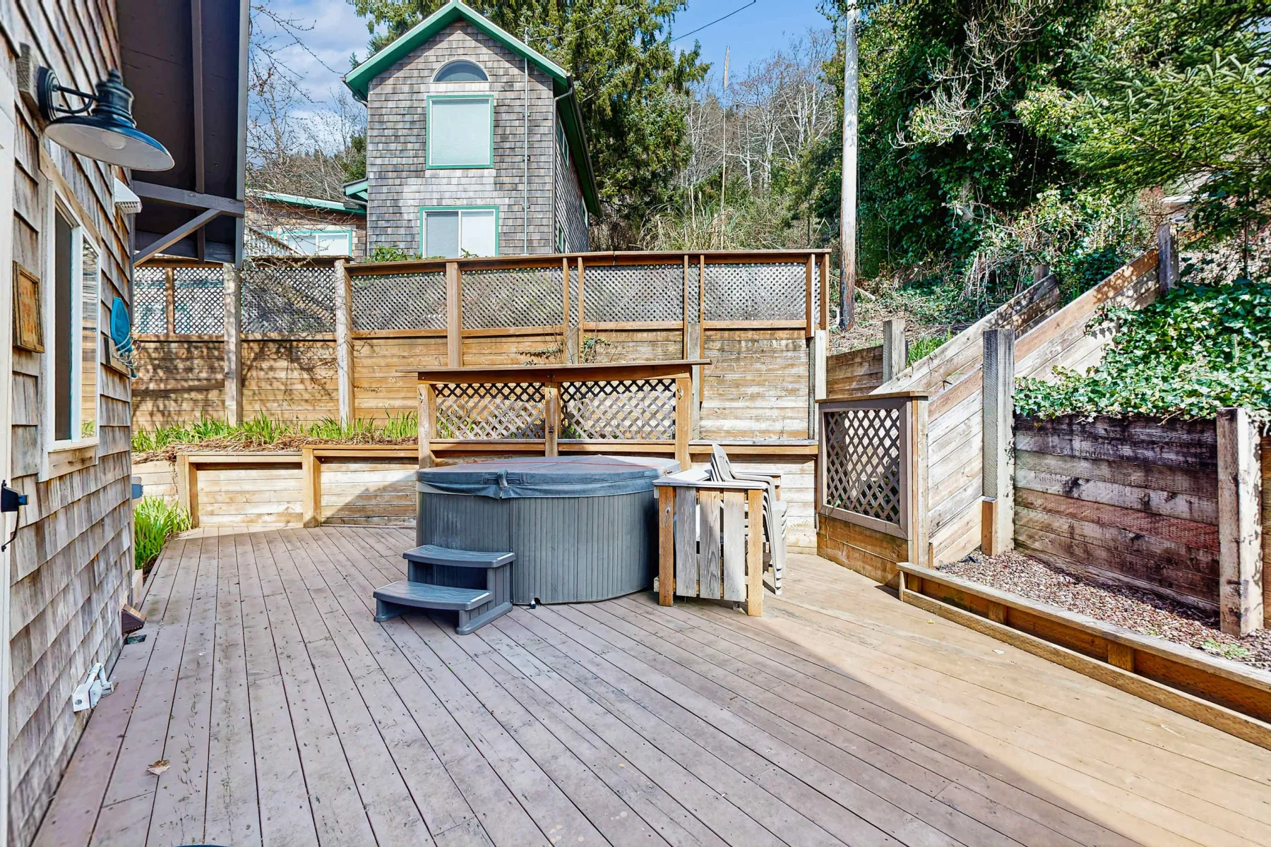 A wooden deck with an outdoor hot tub and fenced seating area.