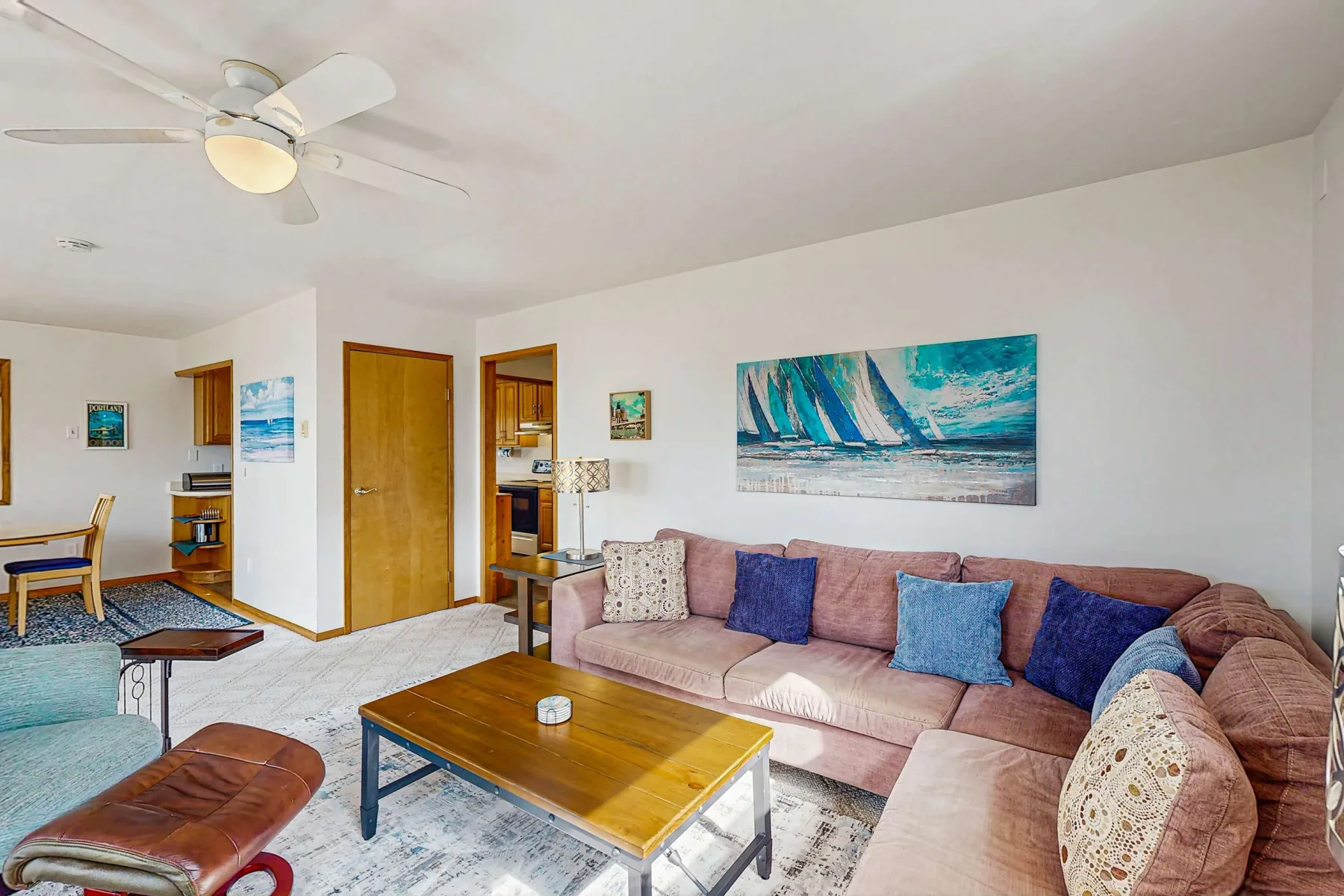 A living room with seating around a wooden coffee table and a colorful ocean-themed wall picture.