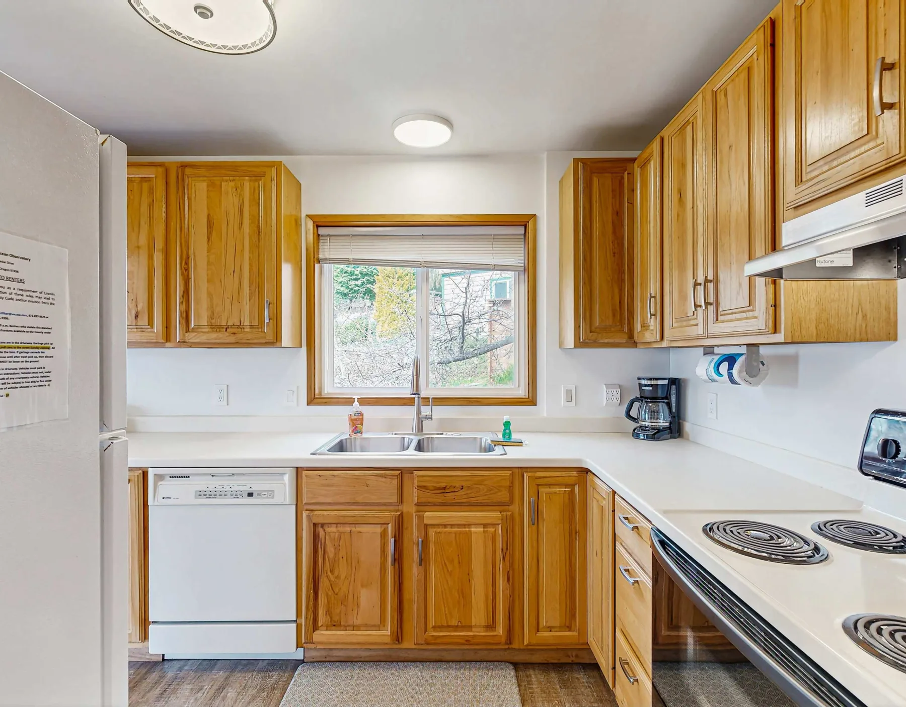 A kitchen with wooden cabinets, white countertops, and a window above the sink.