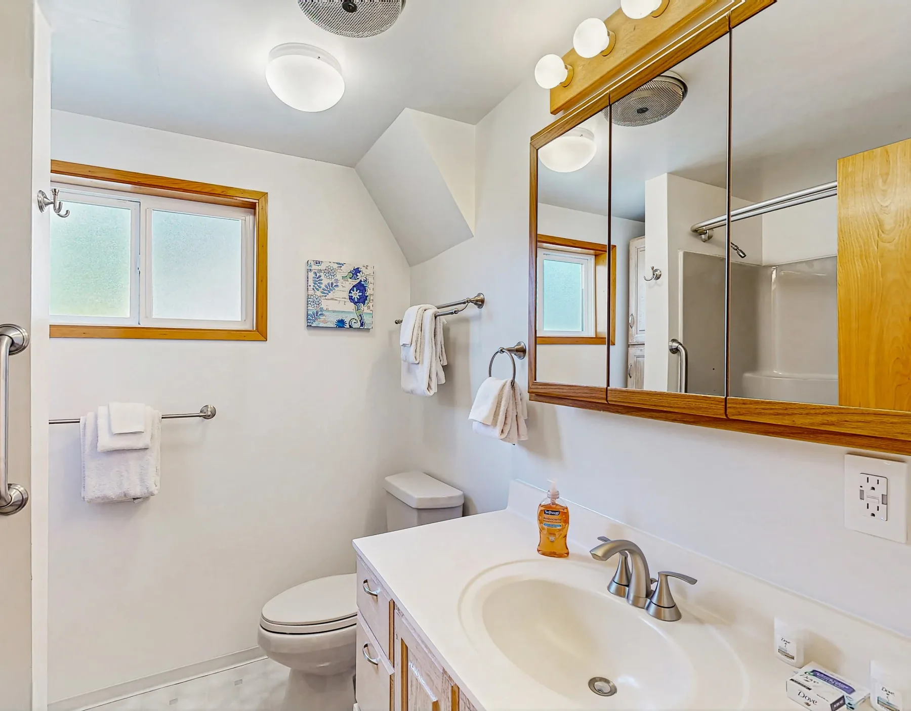 A bright bathroom with a sink, mirror, and shower.