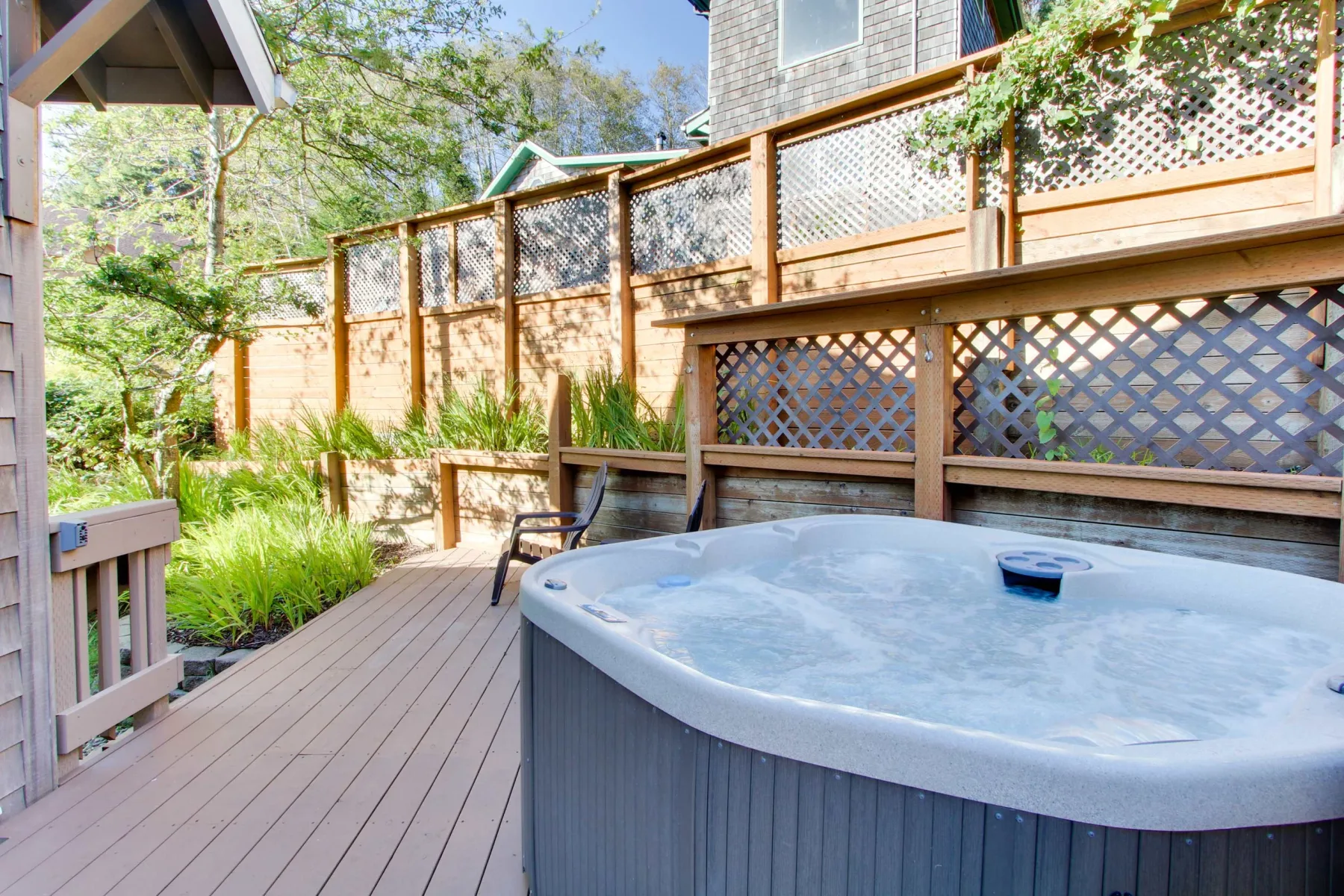 A wooden deck with a large hot tub beside a lattice fence.