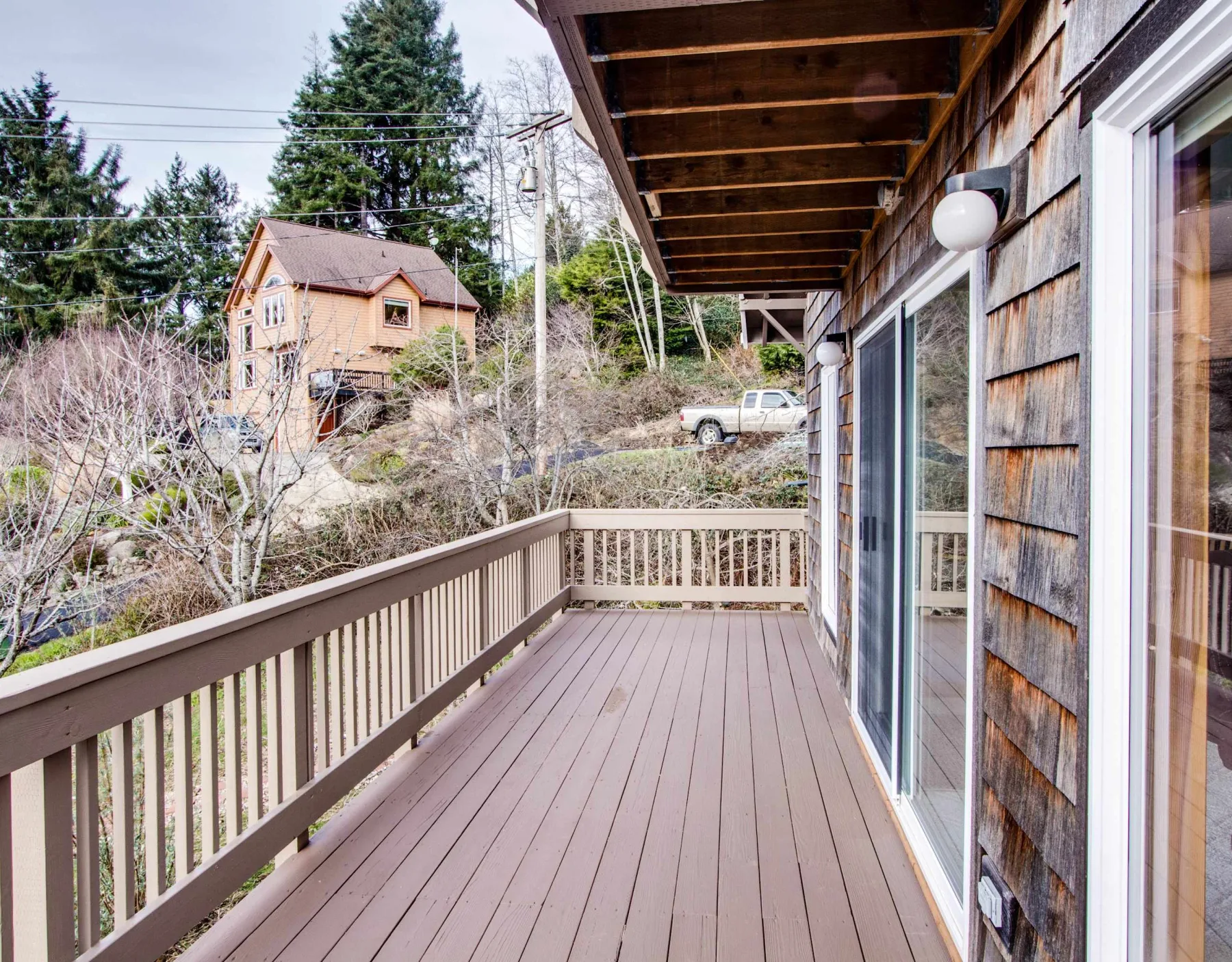 A wooden deck runs alongside the house, with railings and sliding glass doors.