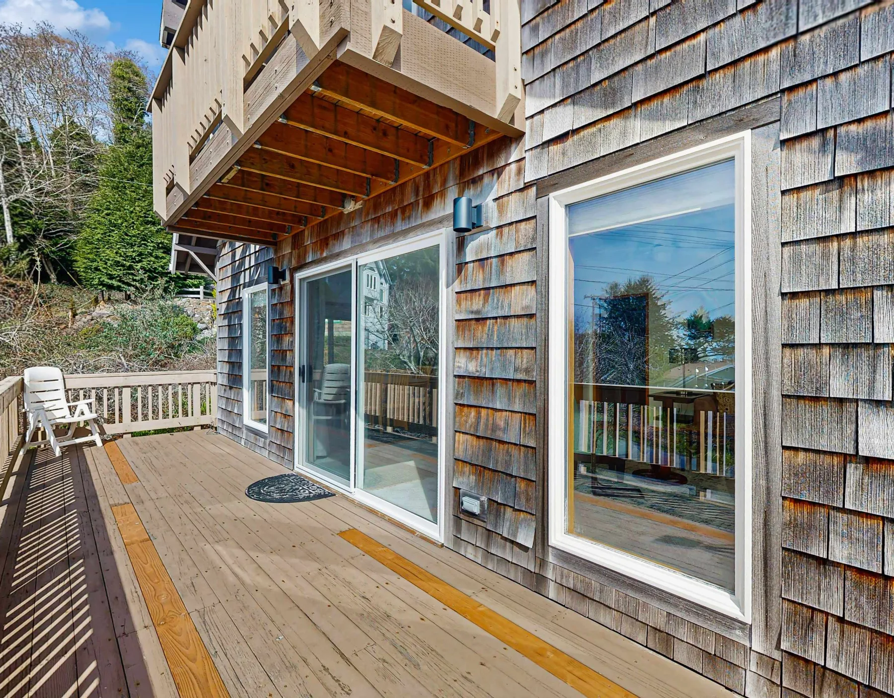 An exterior wooden deck runs alongside a shingled house with large windows.