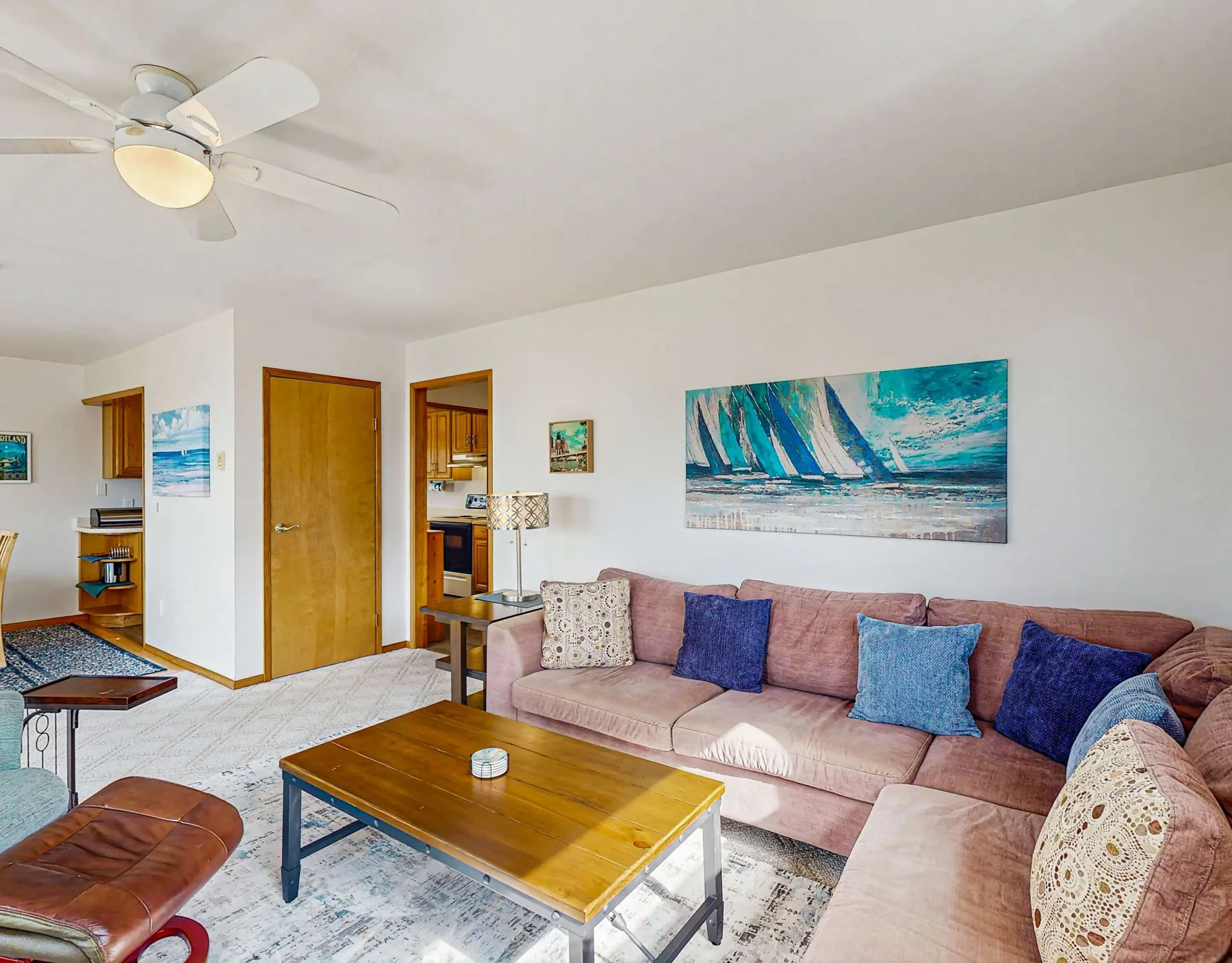 A living room with a pink sectional sofa, a wooden coffee table, and colorful wall art.
