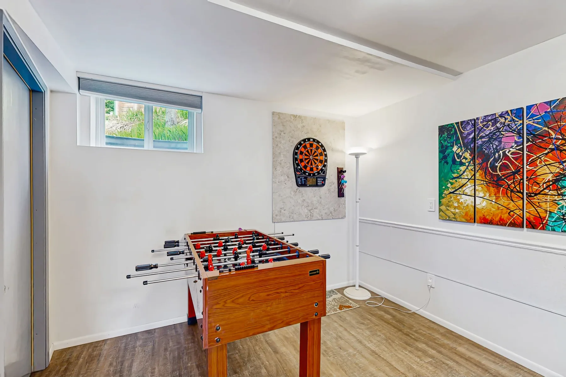 A game room with a foosball table, dartboard, and colorful wall art.
