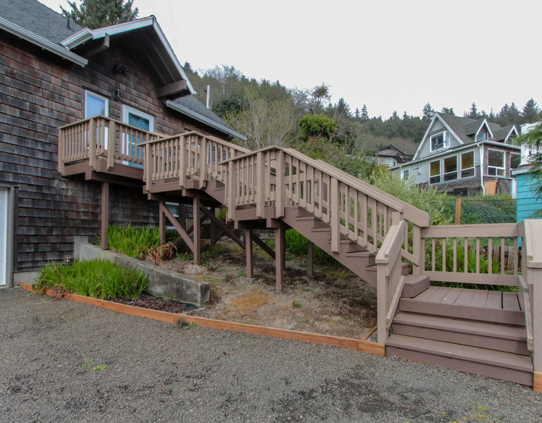 A raised wooden deck and staircase beside a shingled house.
