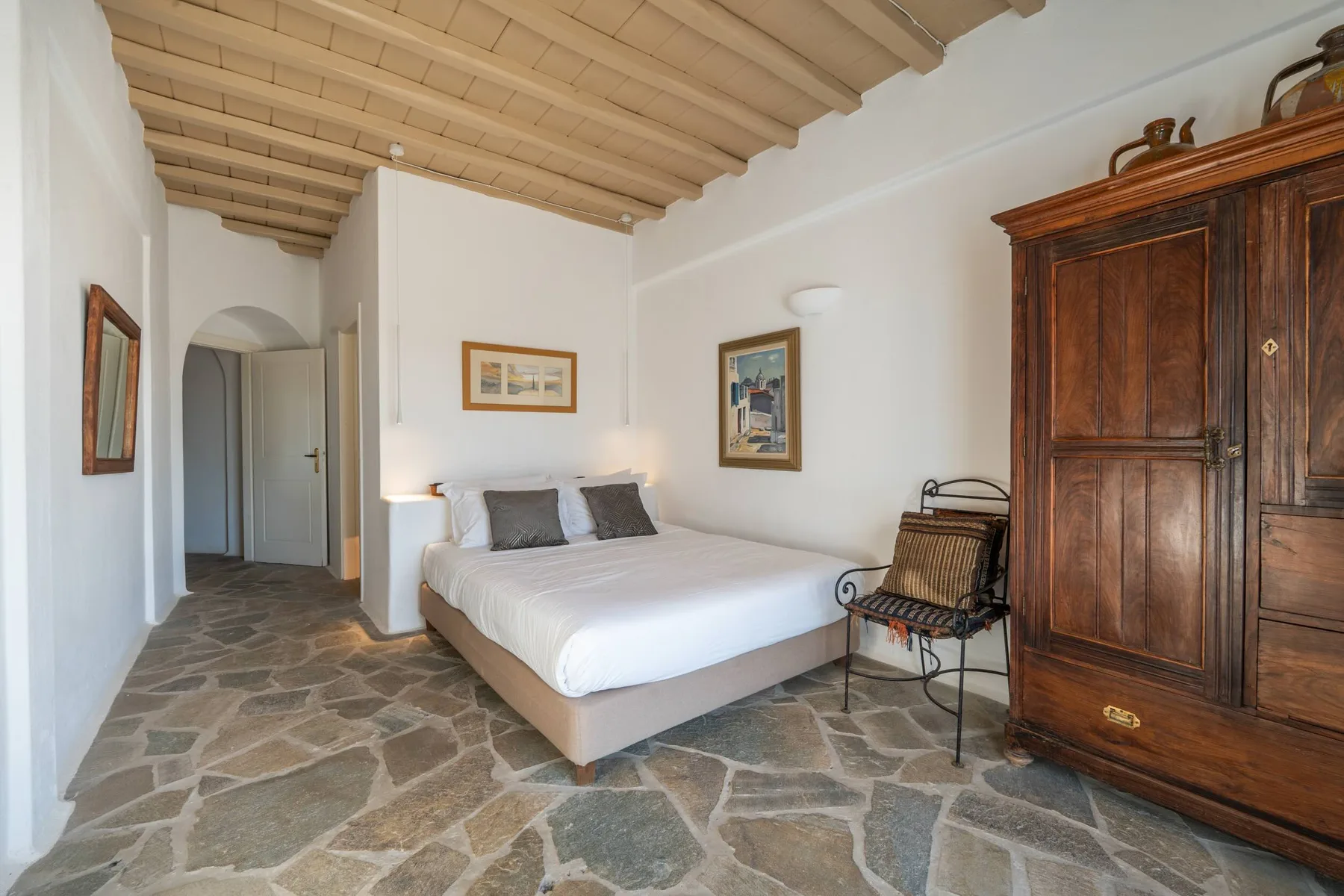 A bedroom with a bed, a wooden wardrobe, and stone-patterned flooring.
