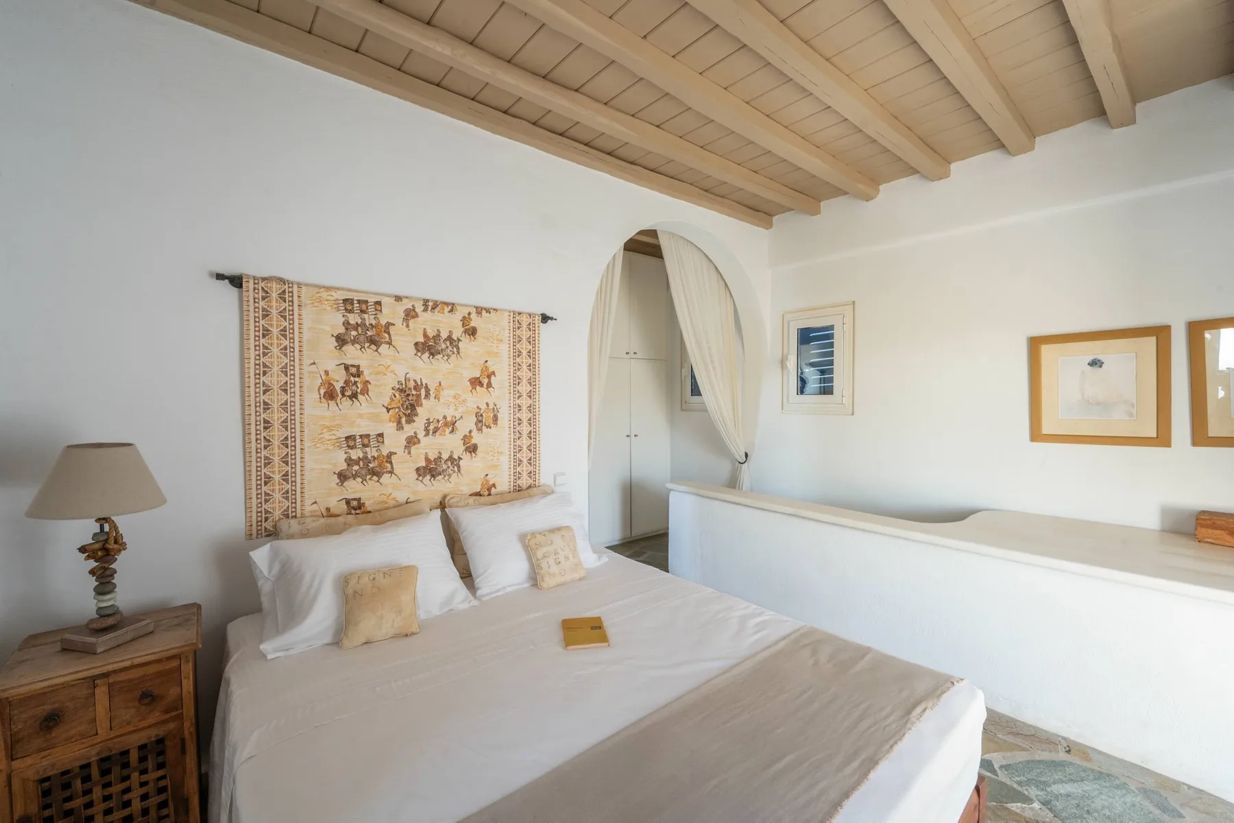 A bright bedroom with a bed beneath a decorative wall hanging.