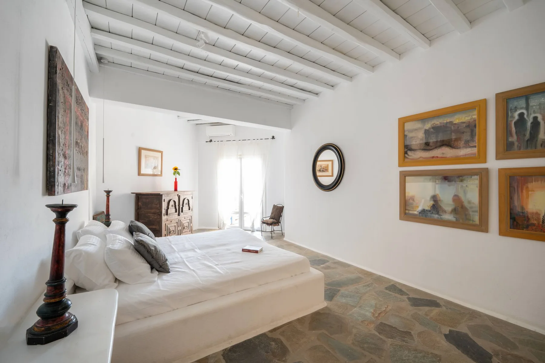 A bright bedroom with a bed beneath exposed white ceiling beams.