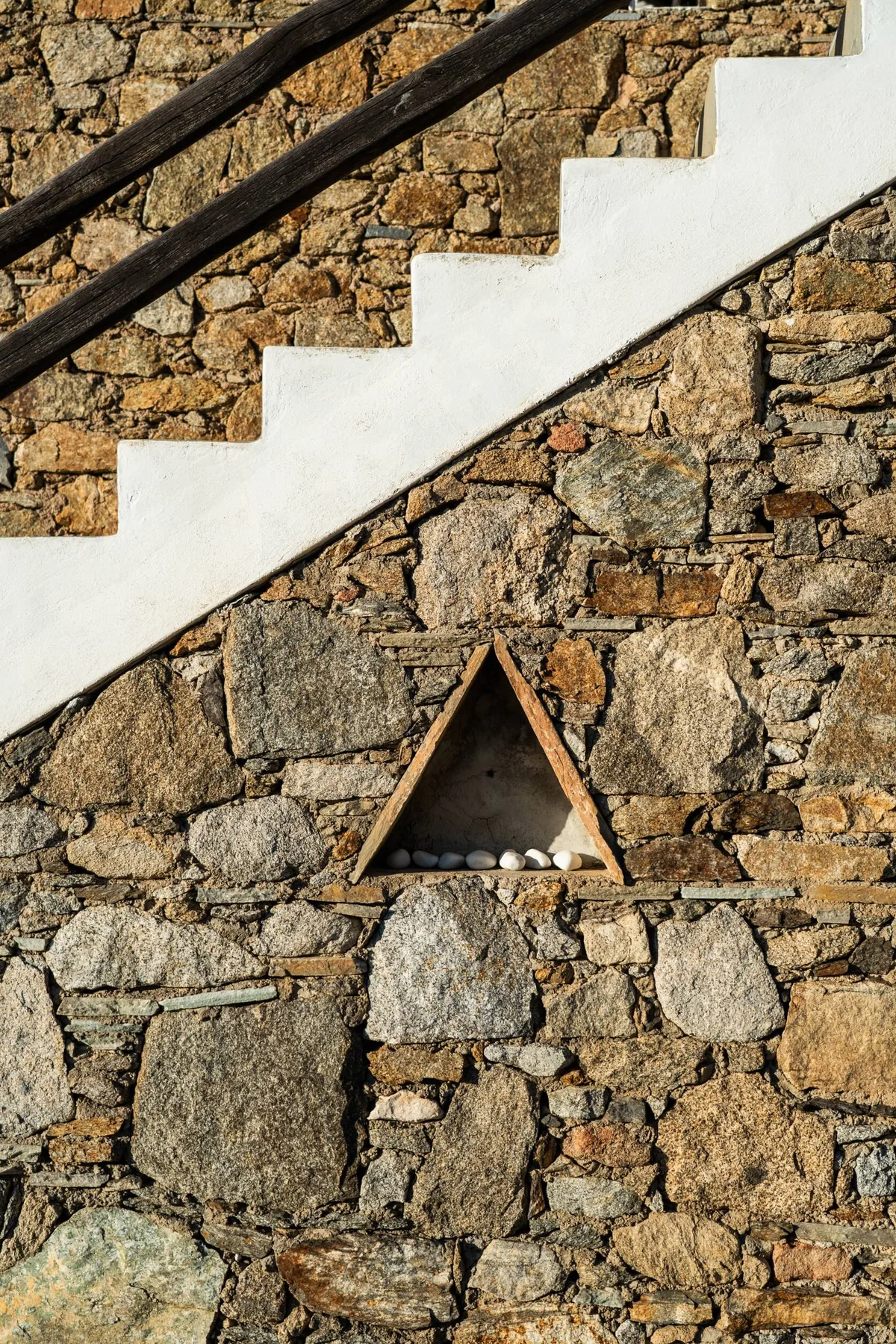 A stone wall with a white staircase and a small triangular niche.