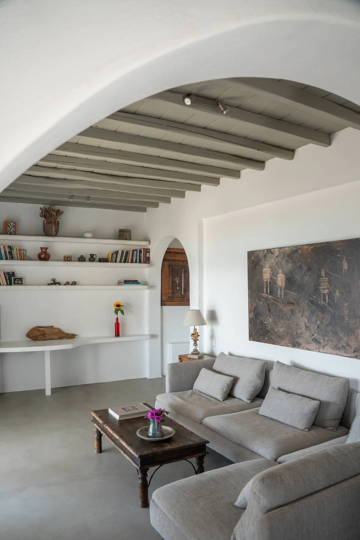 A living room with gray seating, wall shelves, and a large painting.