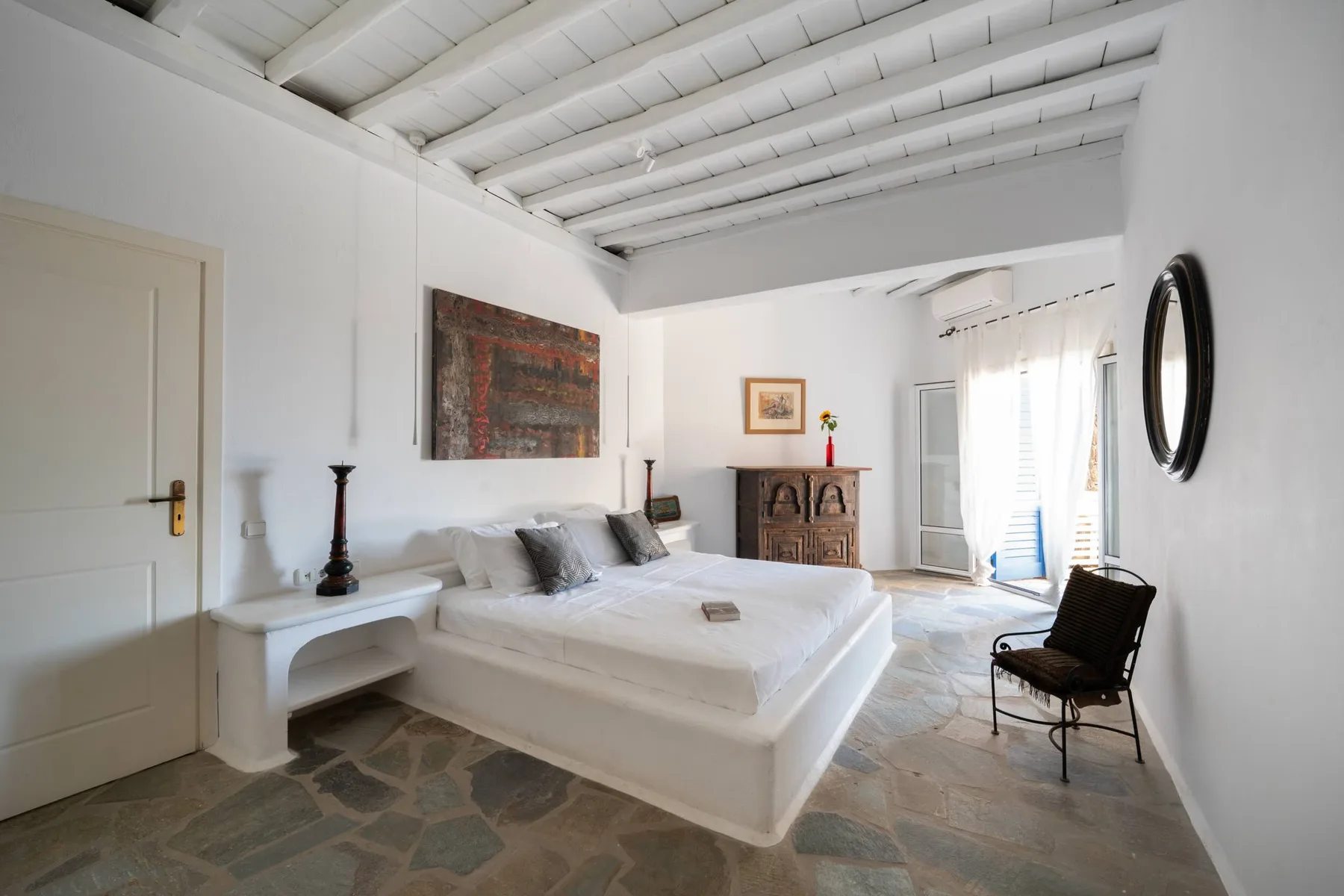 A bright bedroom with a white bed and exposed ceiling beams.