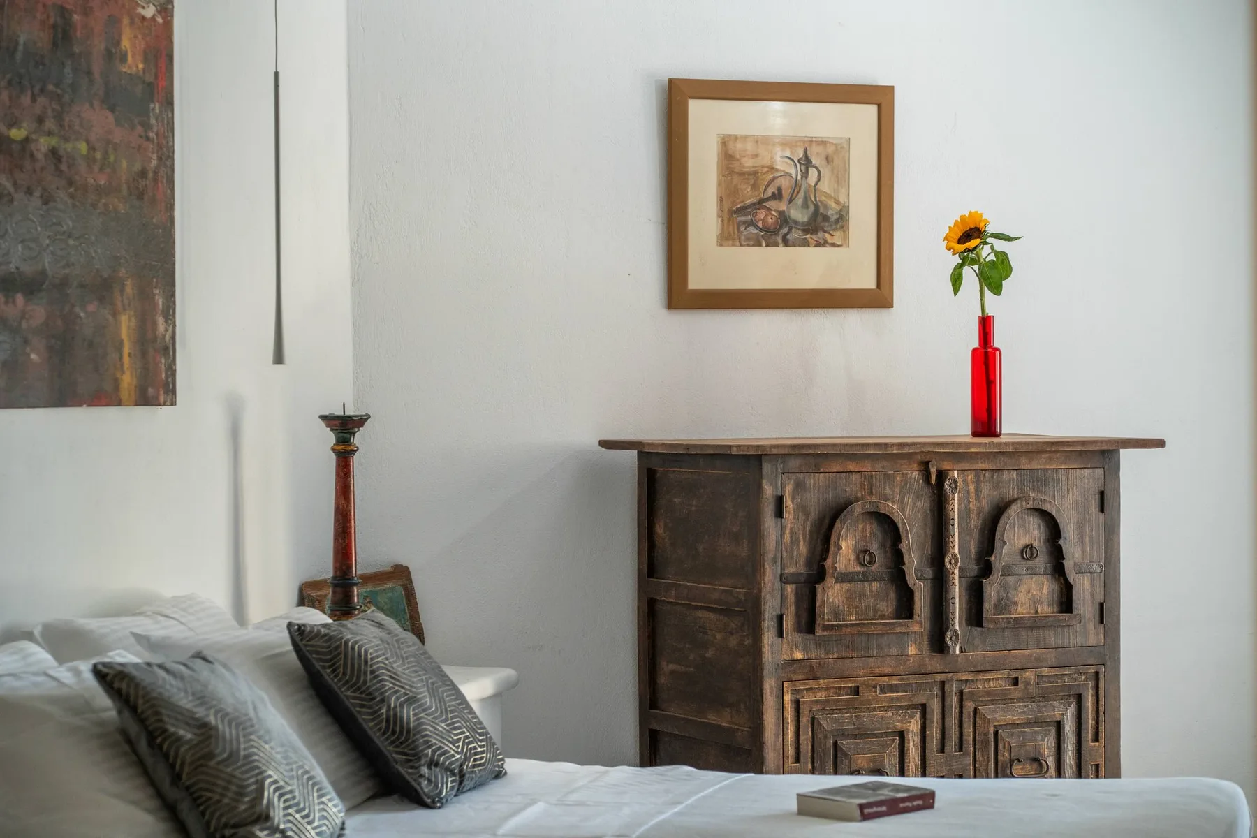 A bedroom with a carved wooden cabinet, framed artwork, and a vase of flowers.