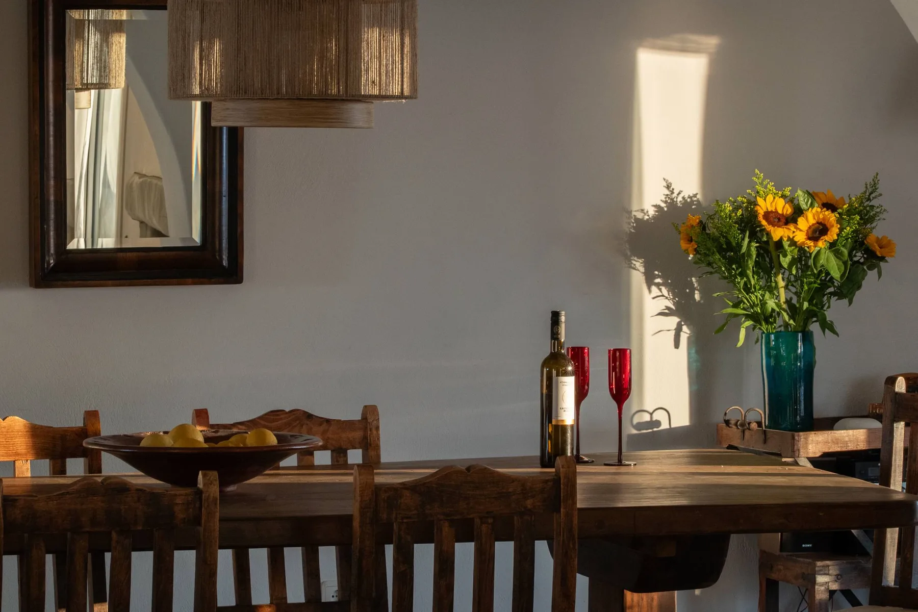 A dining area with a wooden table, wine bottle, and vase of sunflowers.