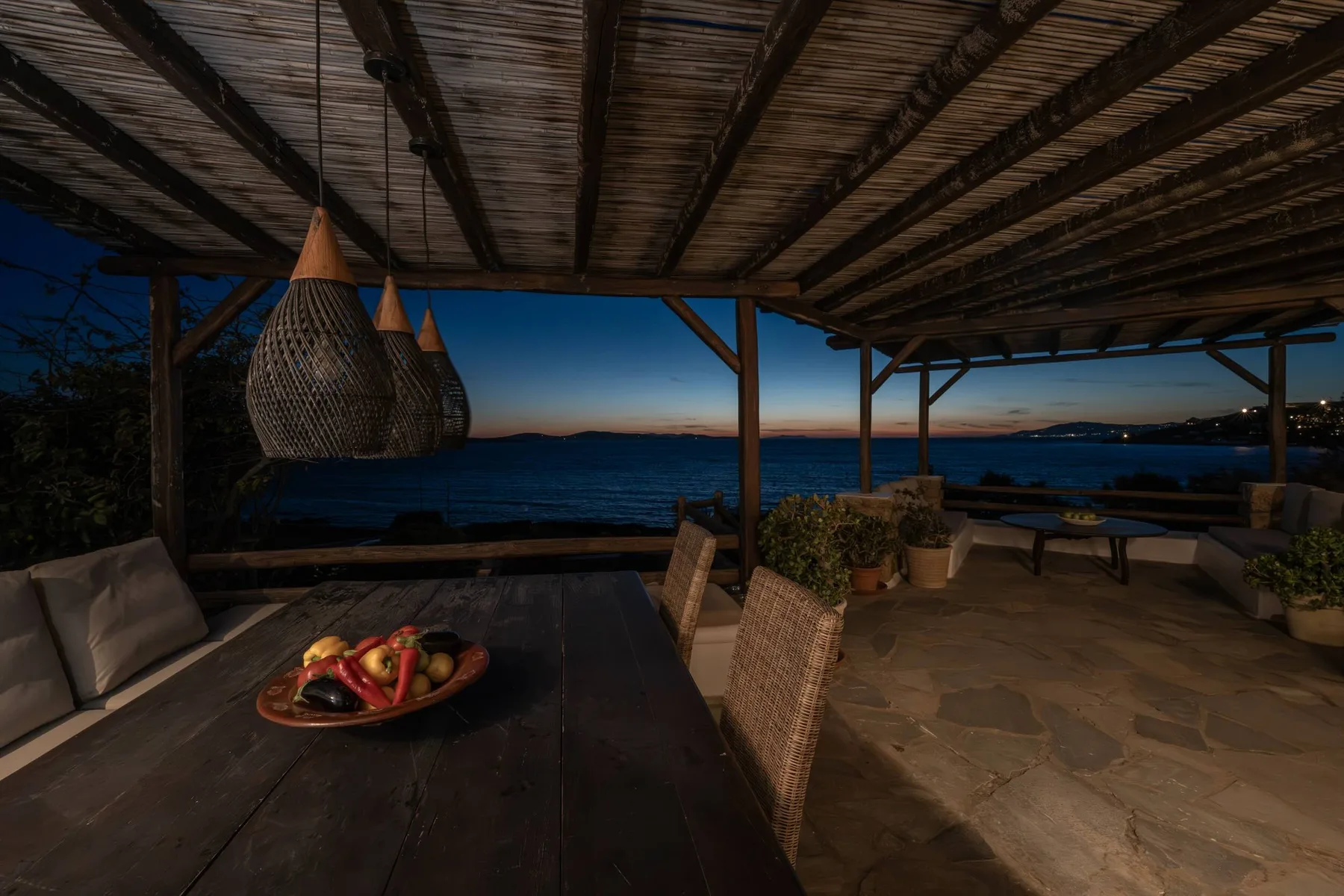A covered outdoor dining area overlooks the water at dusk.