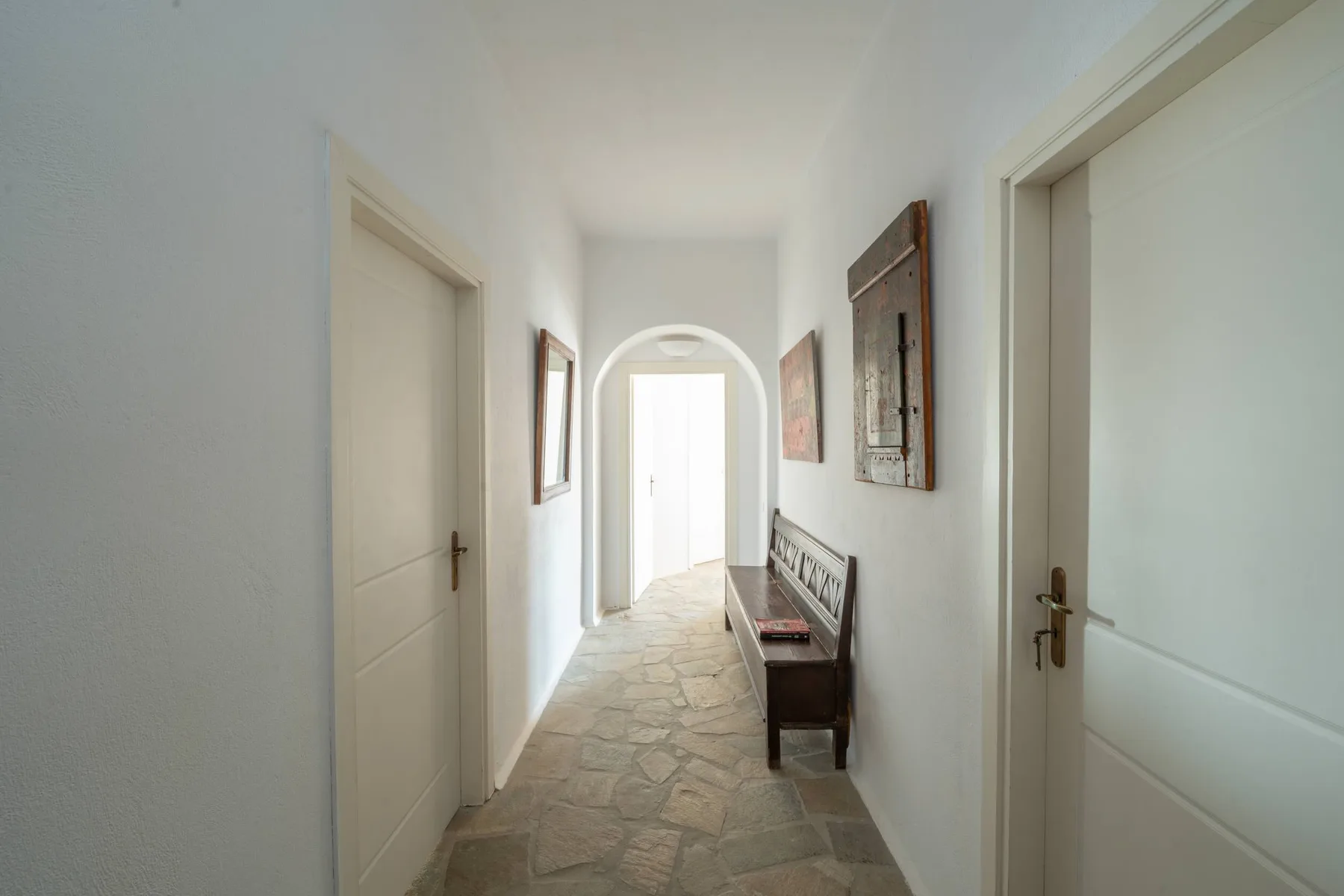 A bright hallway with an arched doorway, wall art, and a wooden bench.
